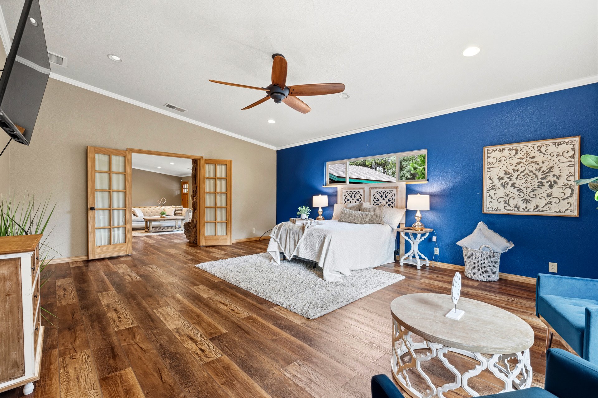 Staged bedroom with a white bed against a blue accent wall and open French doors to a sitting room.