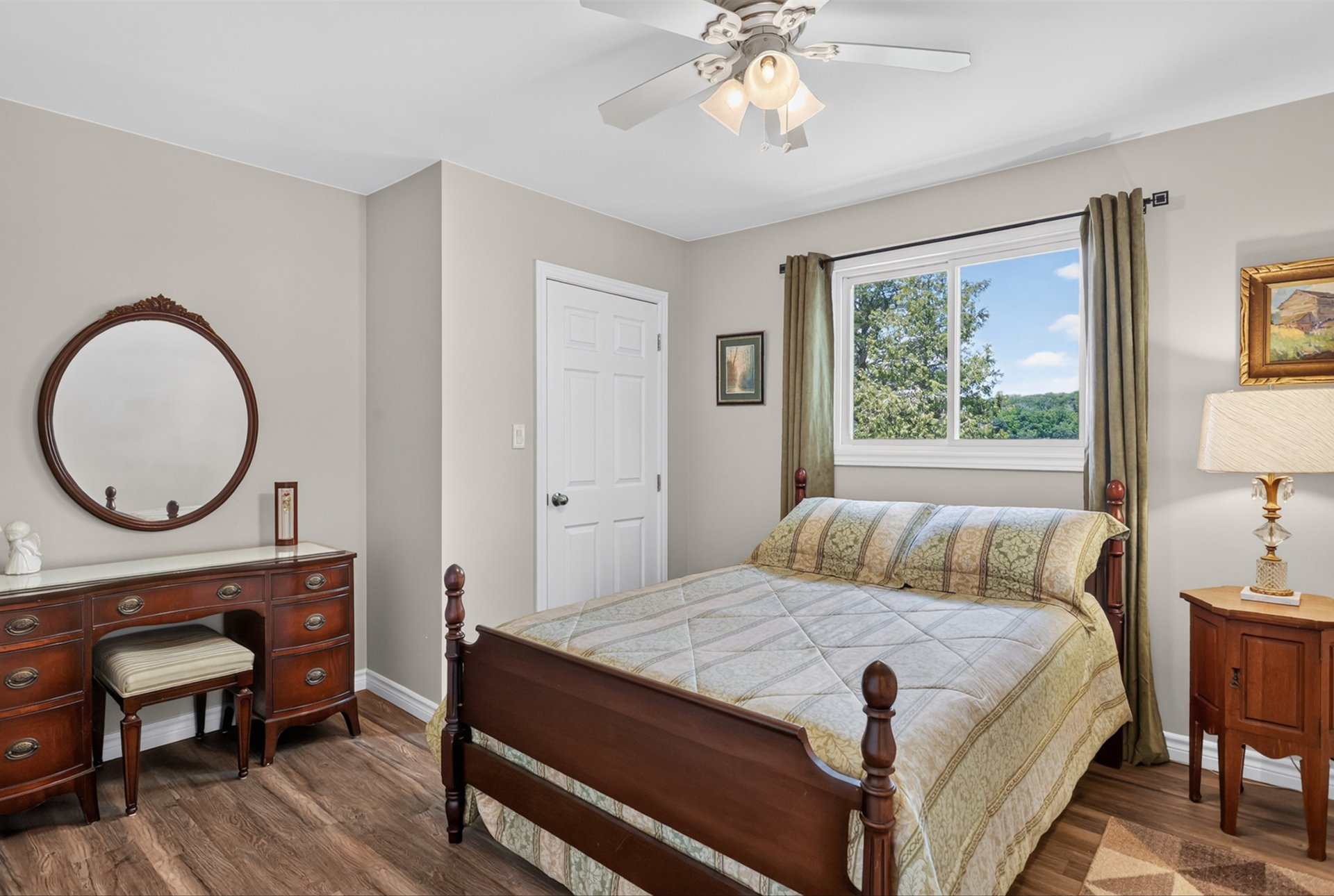 Bedroom with a dark wood four-poster bed and a window overlooking trees and distant hills.