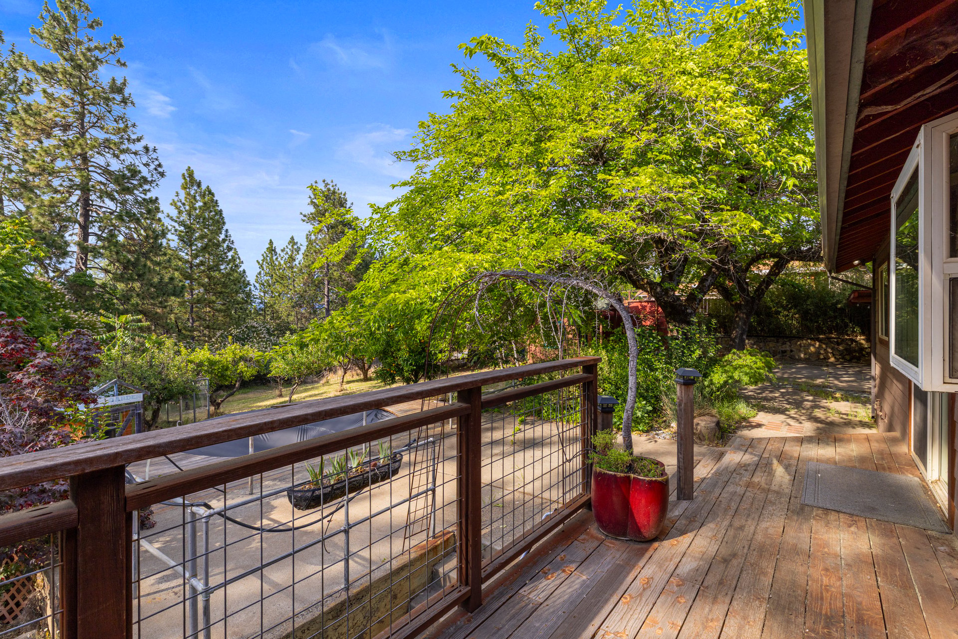 Wooden deck overlooking a leafy yard, with potted plants and an arched garden trellis.