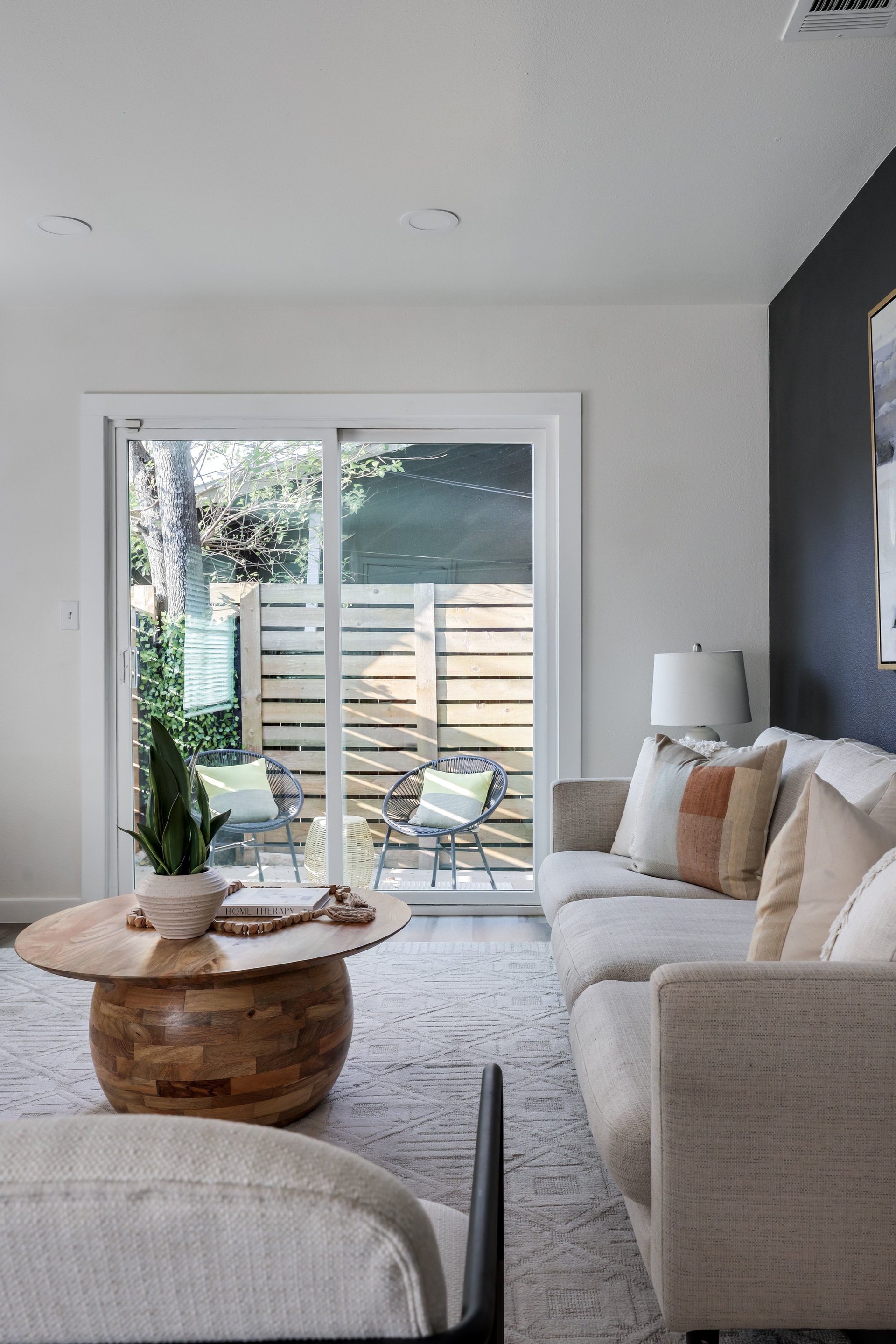 Living room with a light sectional and wood coffee table beside sliding doors to a fenced patio.