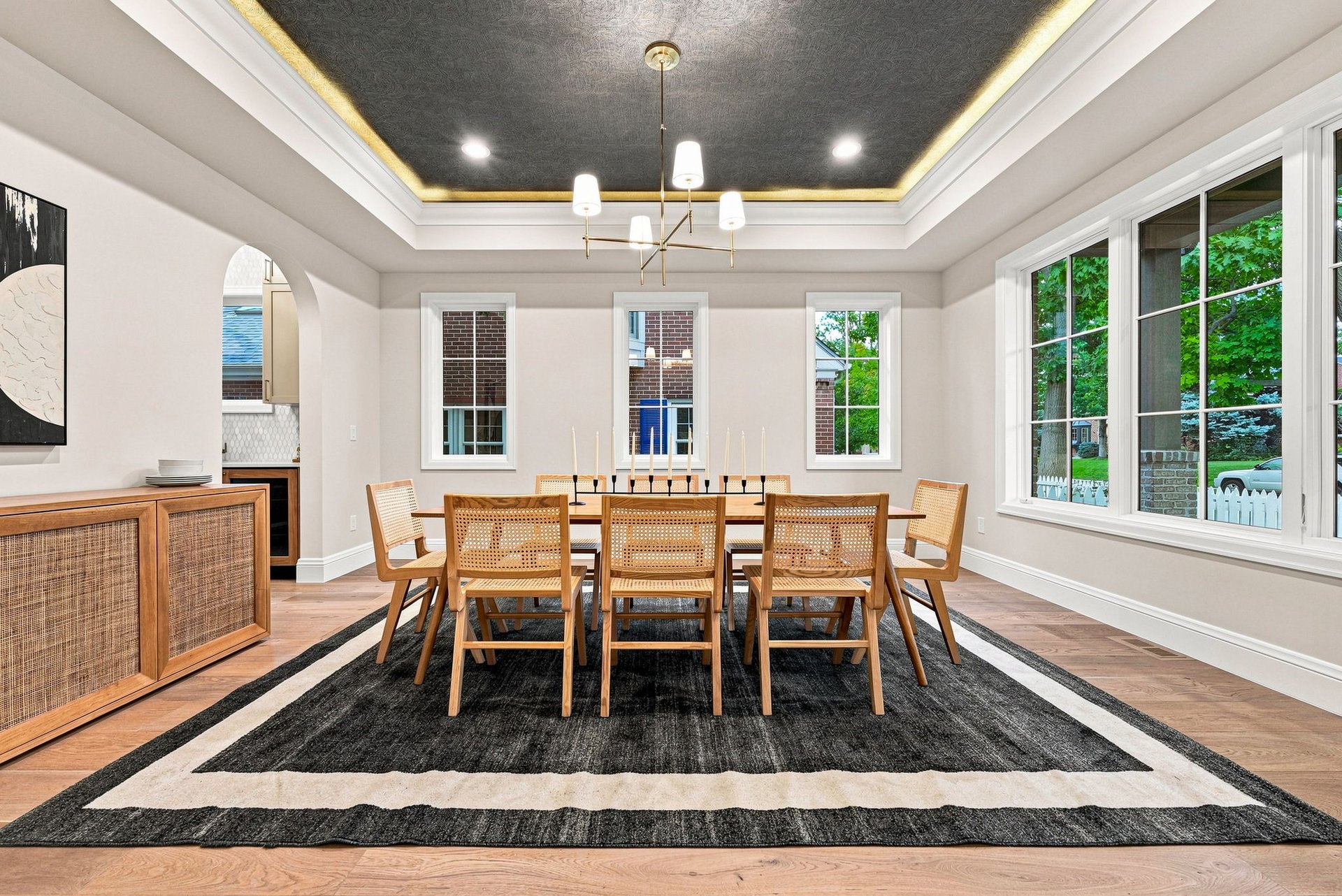 Dining room with a long wooden table, woven chairs, and a dark coffered ceiling with gold trim.