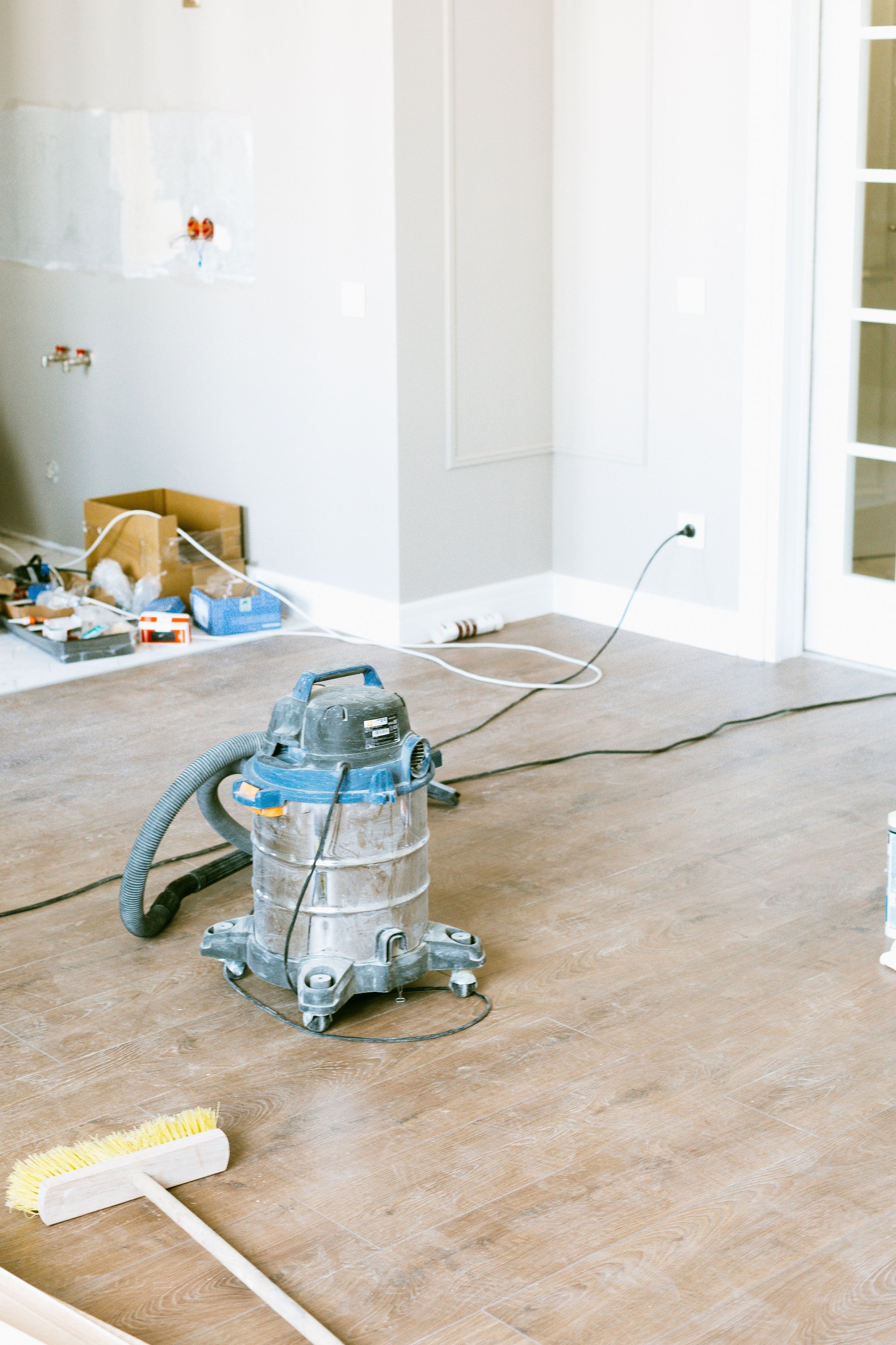 Unfinished room with wood-look flooring, a shop vacuum, and a broom during renovation.