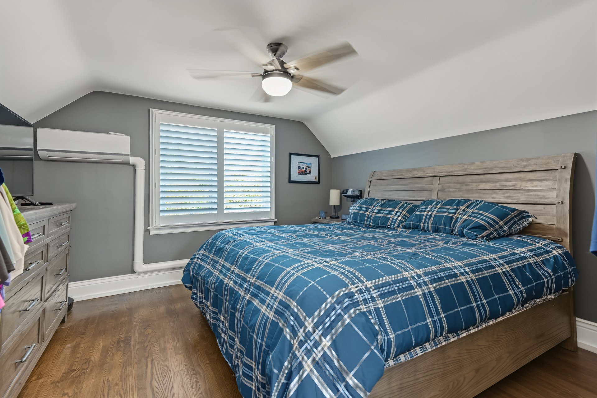 Bedroom with a large wooden bed, blue plaid bedding, vaulted ceiling, and hardwood floor.