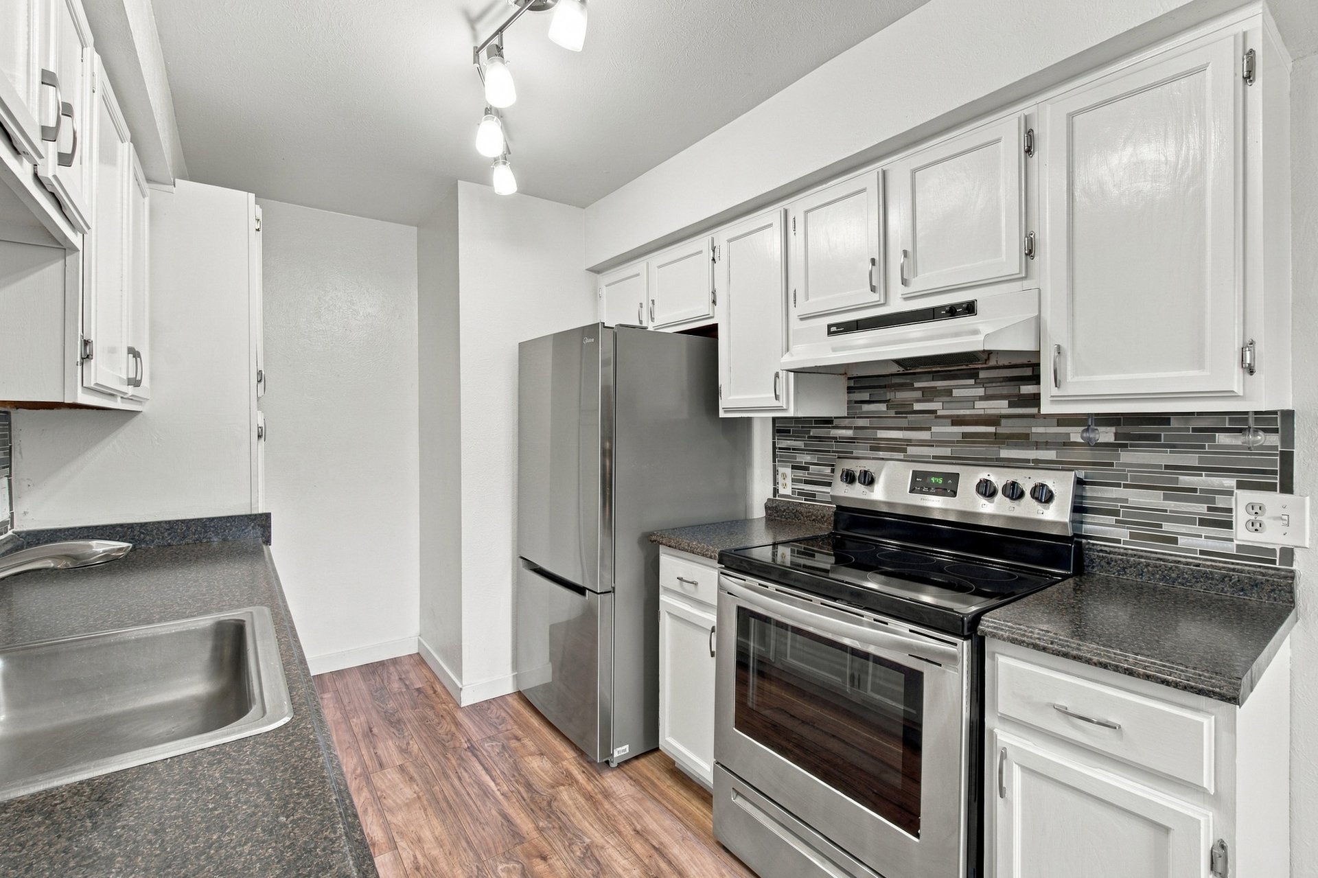 Kitchen with white cabinets, stainless steel appliances, gray tile backsplash, and wood-look flooring.