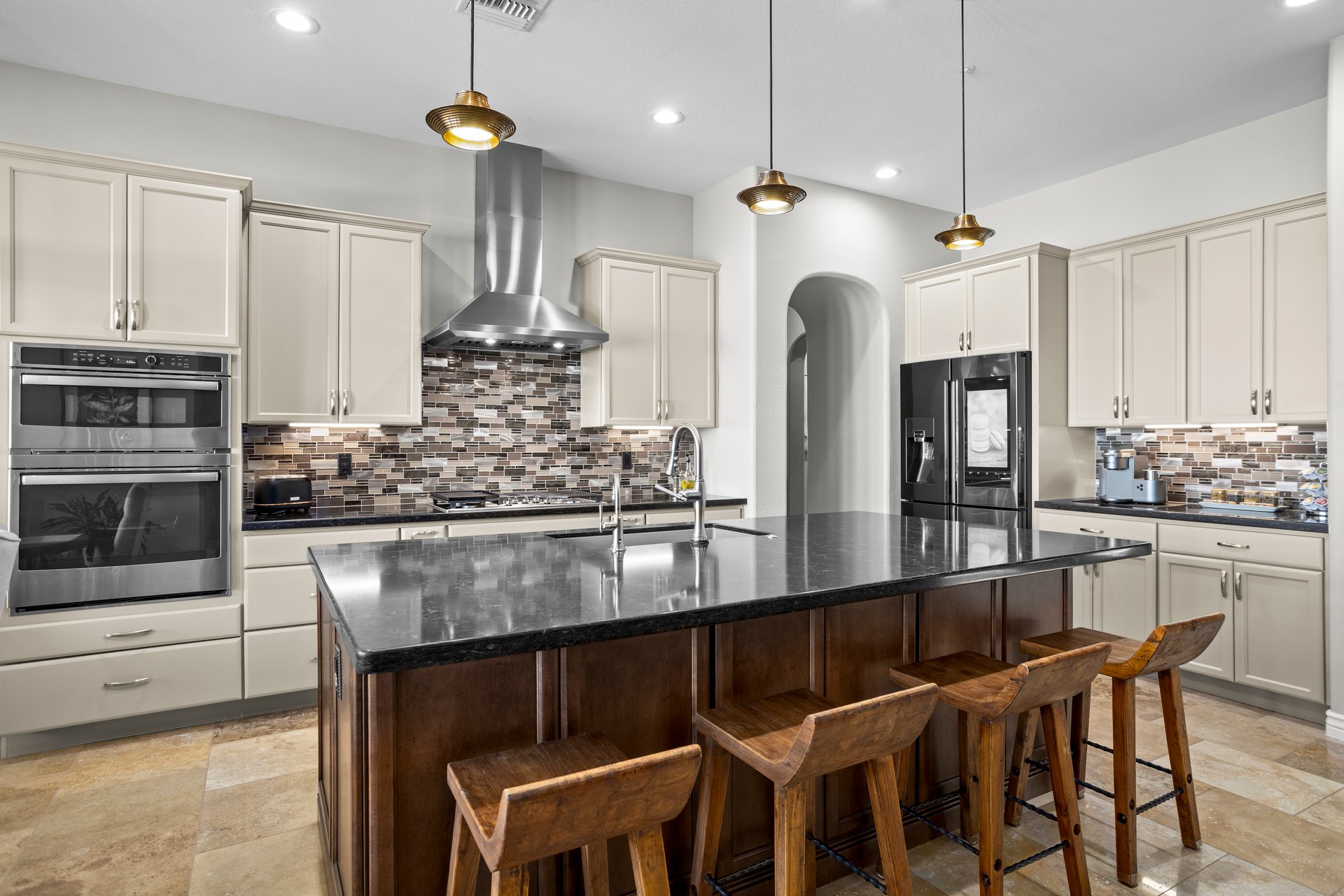 Spacious modern kitchen with a large black island, cream cabinets, stainless steel appliances, mosaic tile backsplash, and bar stools.