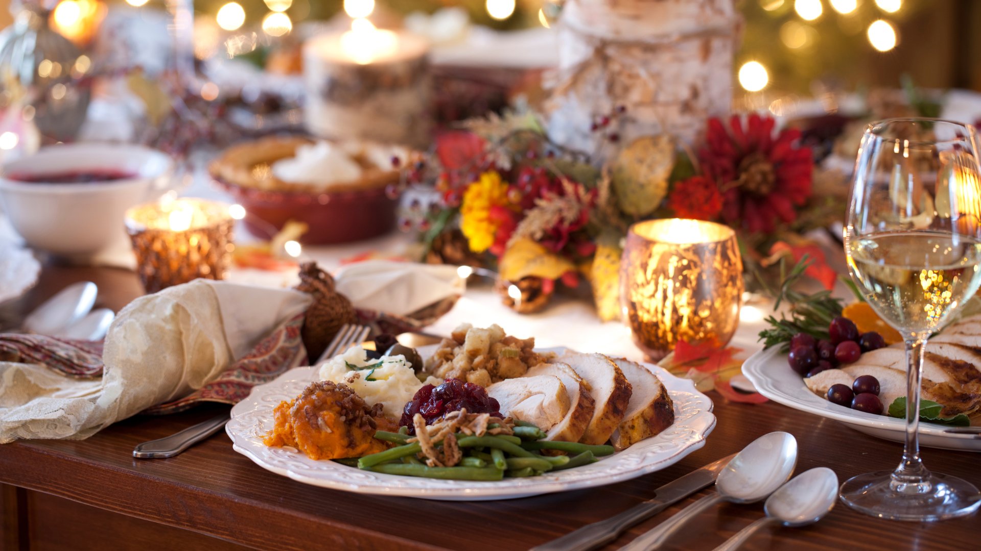 Beautifully arranged Thanksgiving dinner table with sliced turkey cranberry sauce sweet potatoes green beans wine glasses and autumn centerpiece with candles