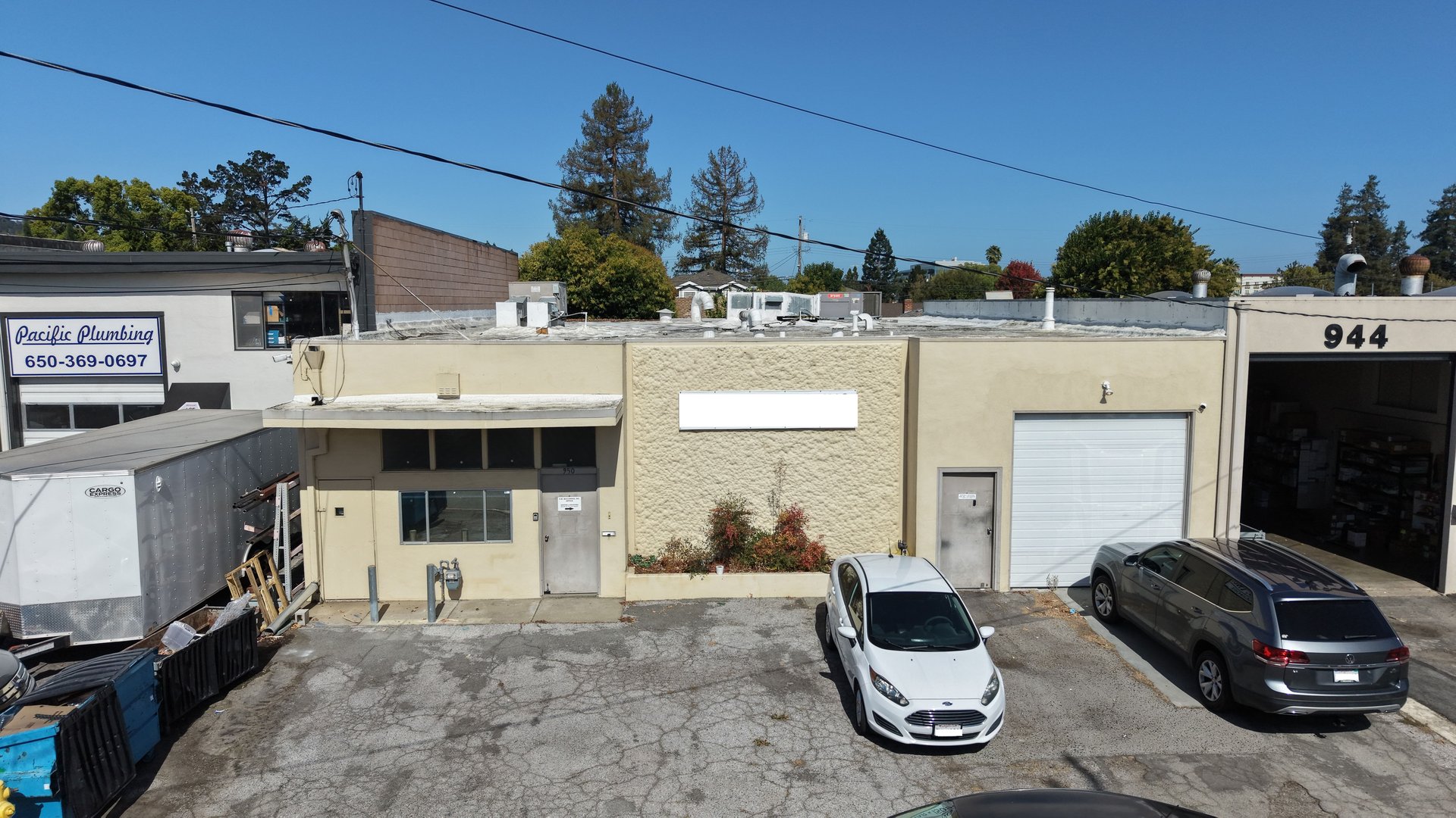 Commercial building with roll-up garage door, open service bay, and two cars parked in front.