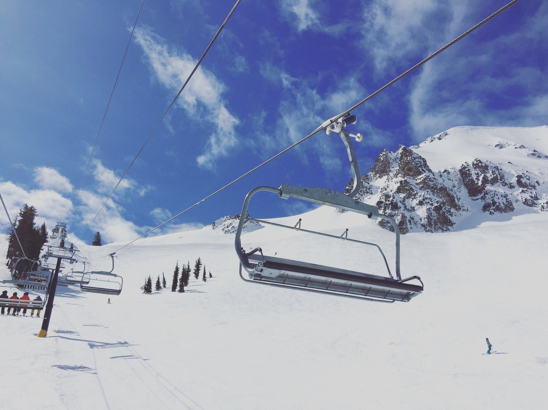 Chairlifts cross a snowy Squaw Valley slope beneath rugged peaks as a skier descends.