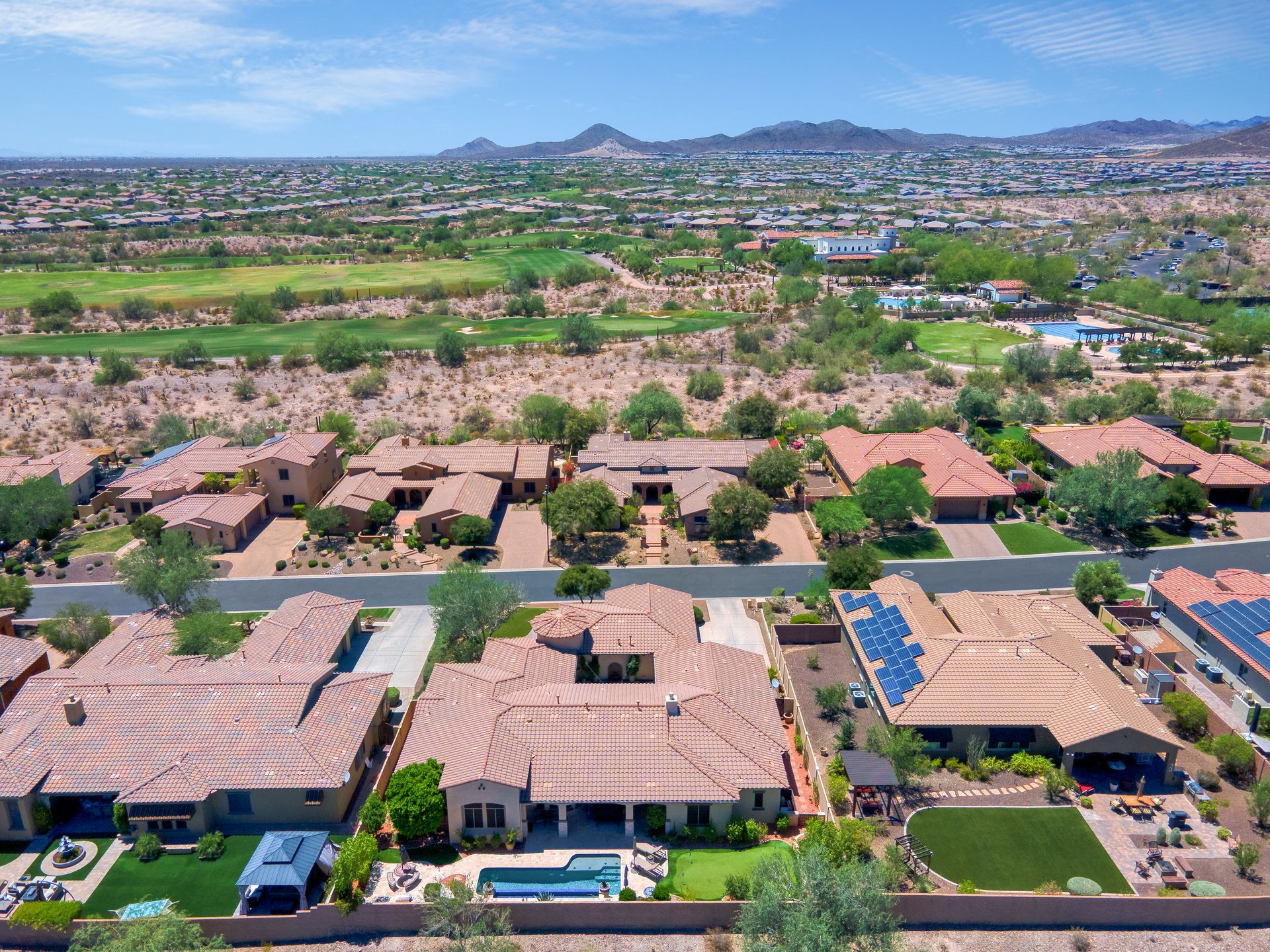 Aerial view of a suburban neighborhood with desert landscaping, golf course, and mountains in the distance.