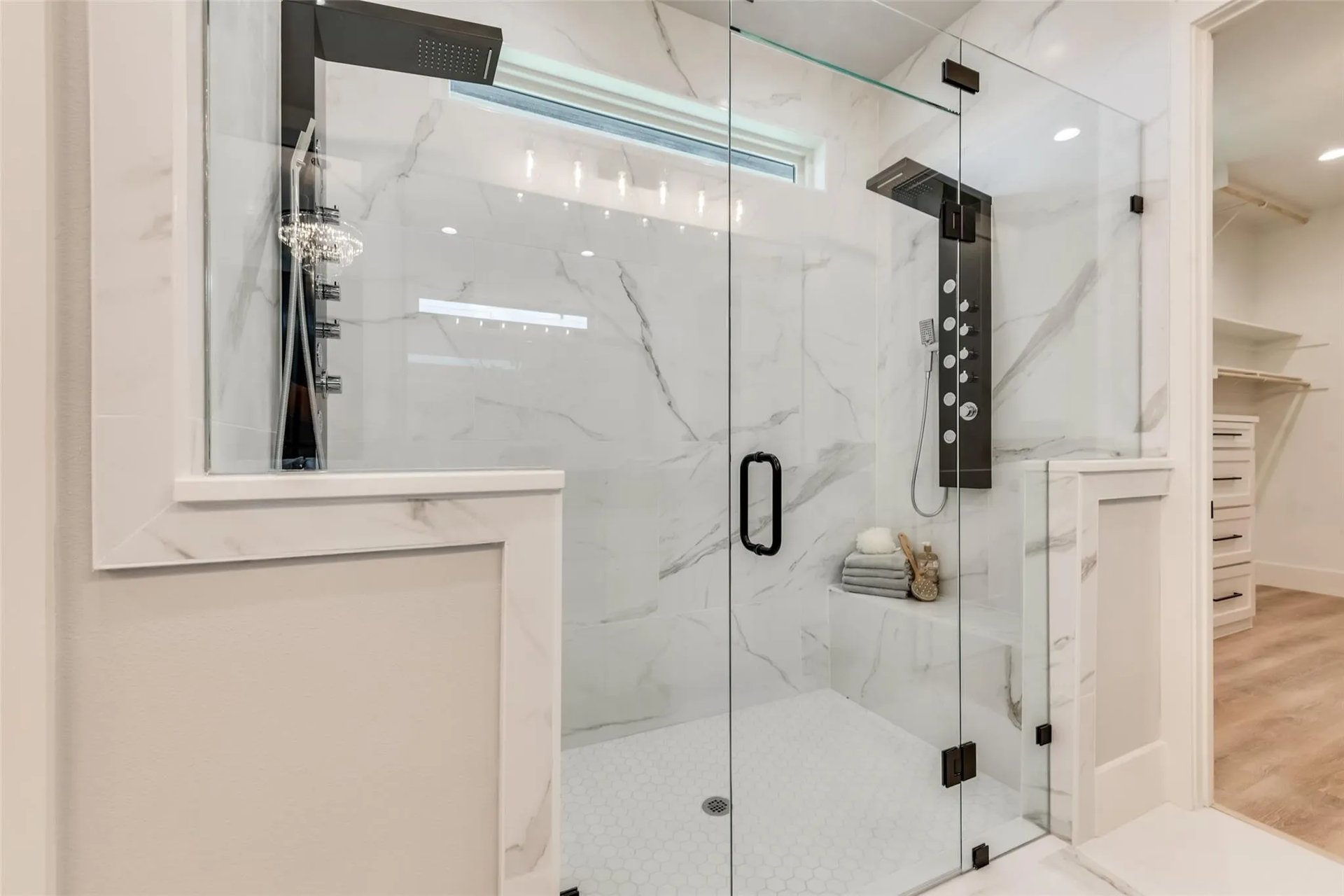 Marble-look walk-in shower with clear glass doors, a built-in bench, and black fixtures.