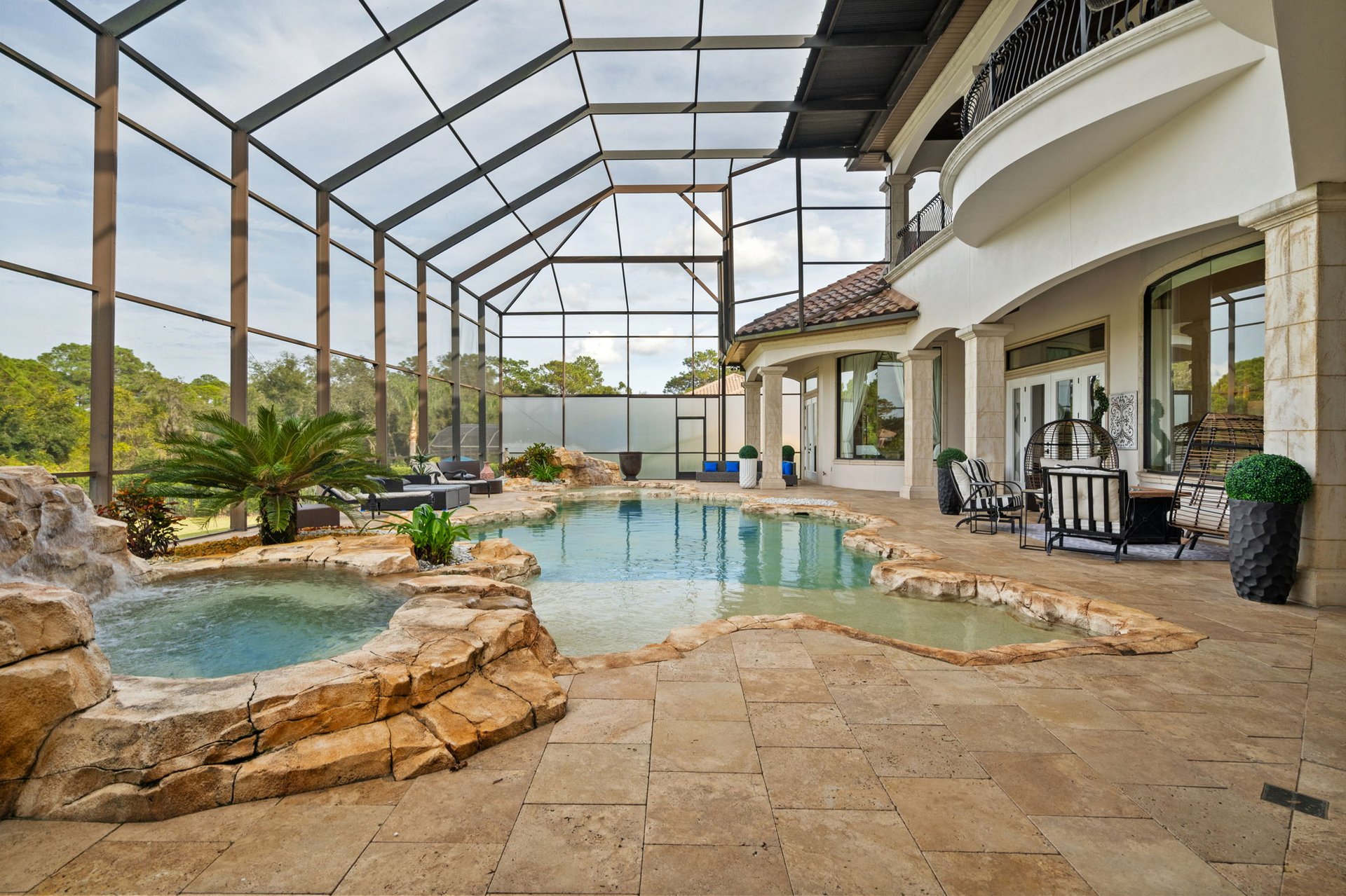 Freeform pool and rock-edged spa beneath a screen enclosure beside a furnished stone patio.