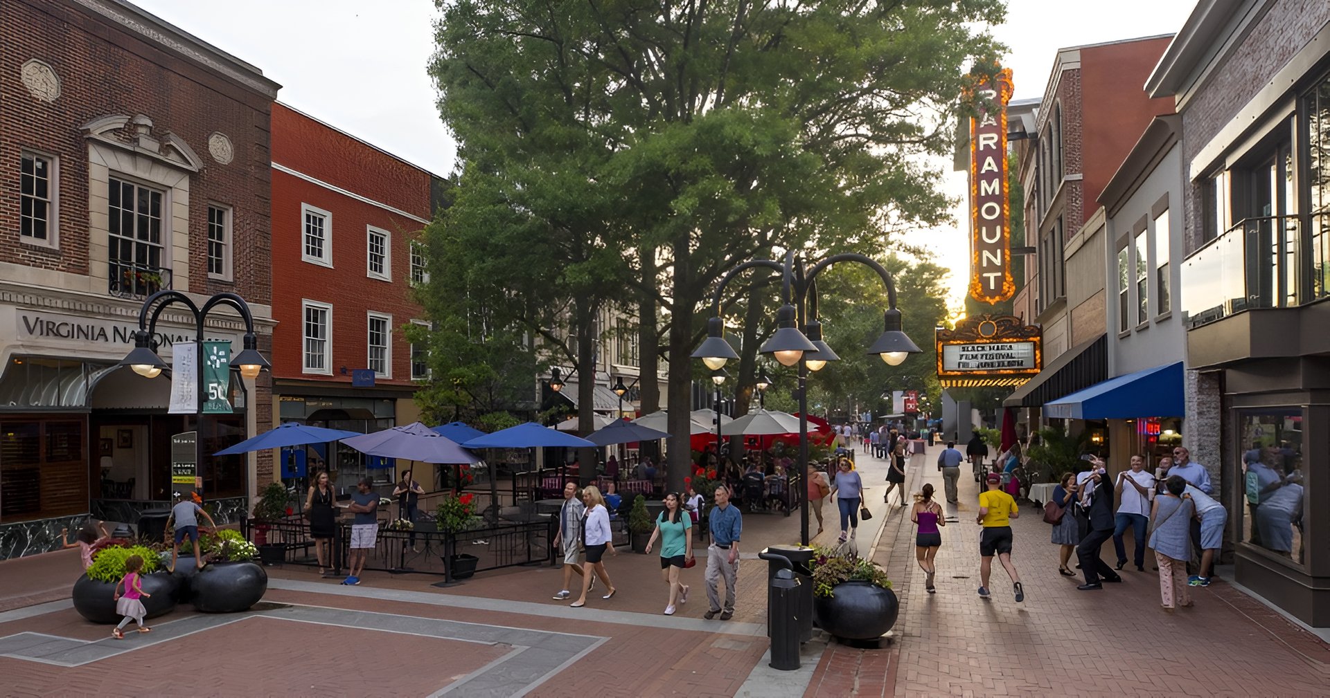Charlottesville Downtown Mall with brick storefronts, outdoor dining, pedestrians, and the illuminated Paramount sign.
