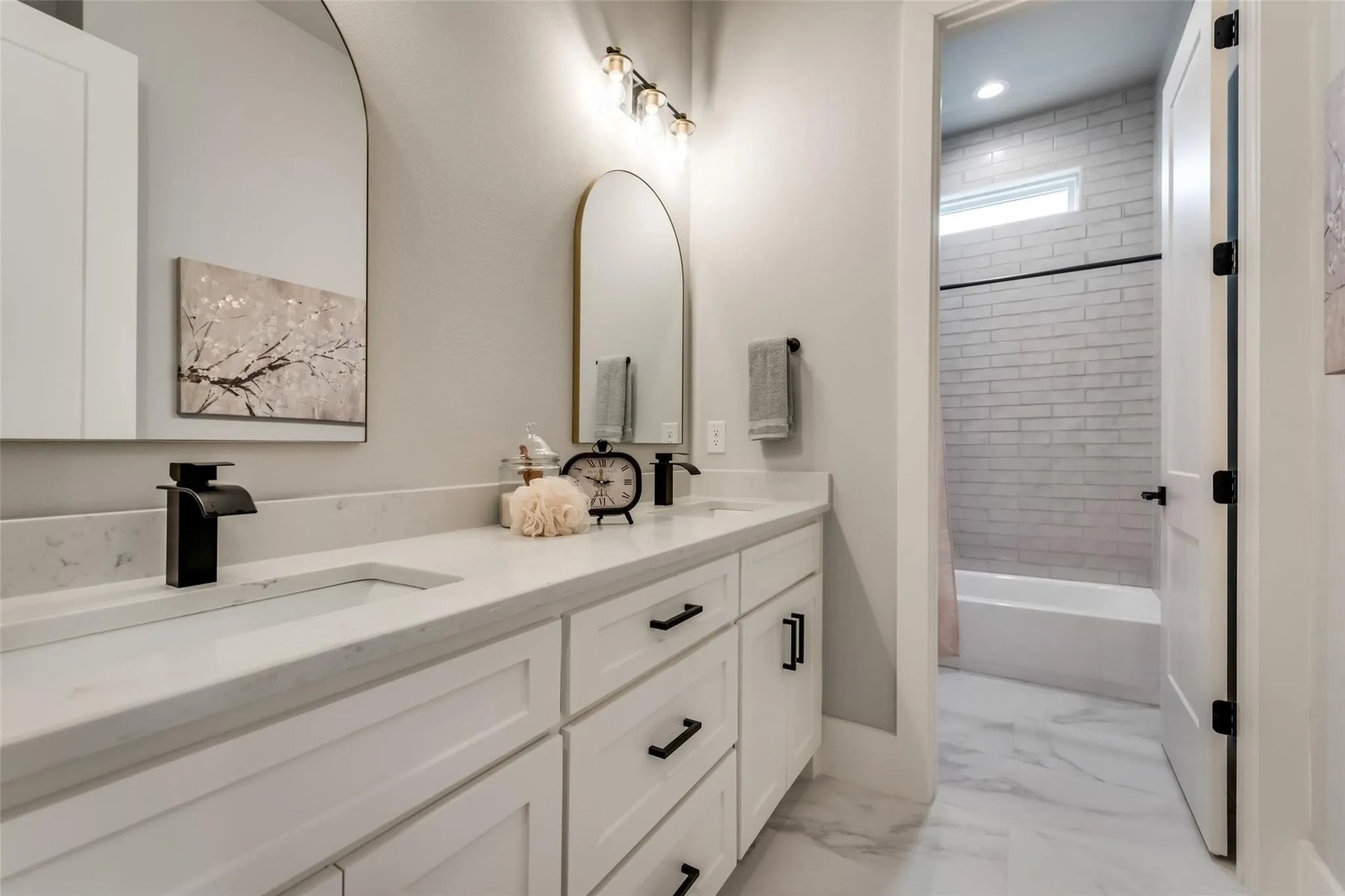 Bathroom with a white double vanity, arched mirror, and adjoining subway-tile tub and shower.