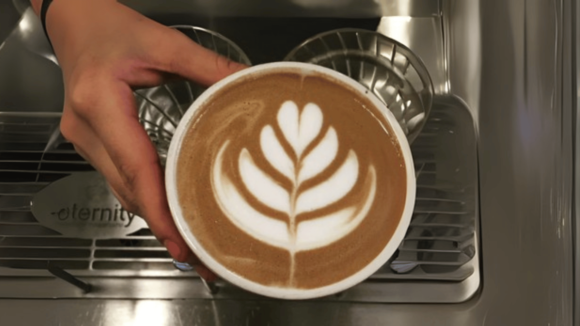 Hand holding perfect rosetta latte art on espresso machine drip tray - Miami's professional barista craftsmanship by The Edit Real Estate