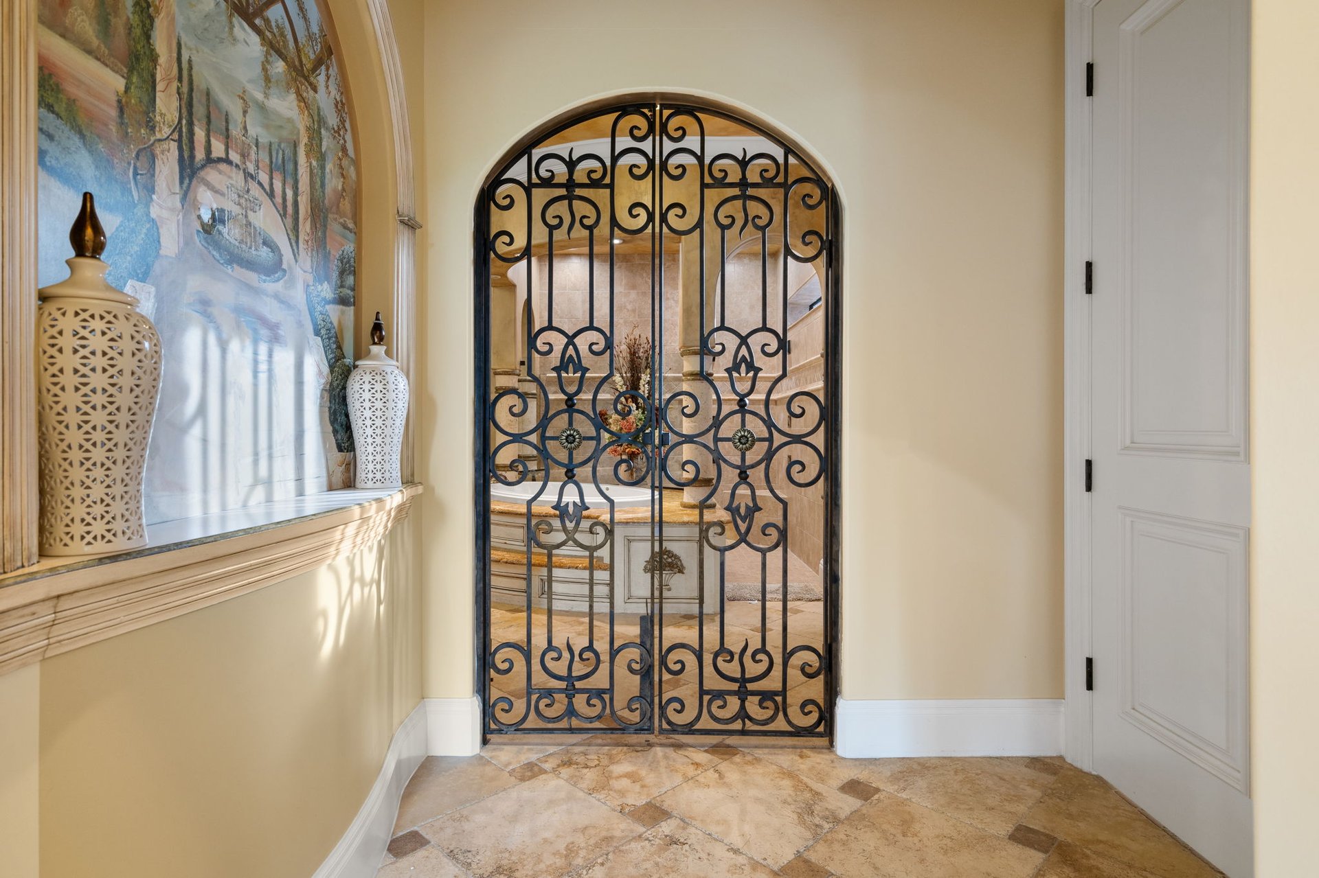 Foyer with an ornate wrought-iron gate, painted mural, and tan tile floor.