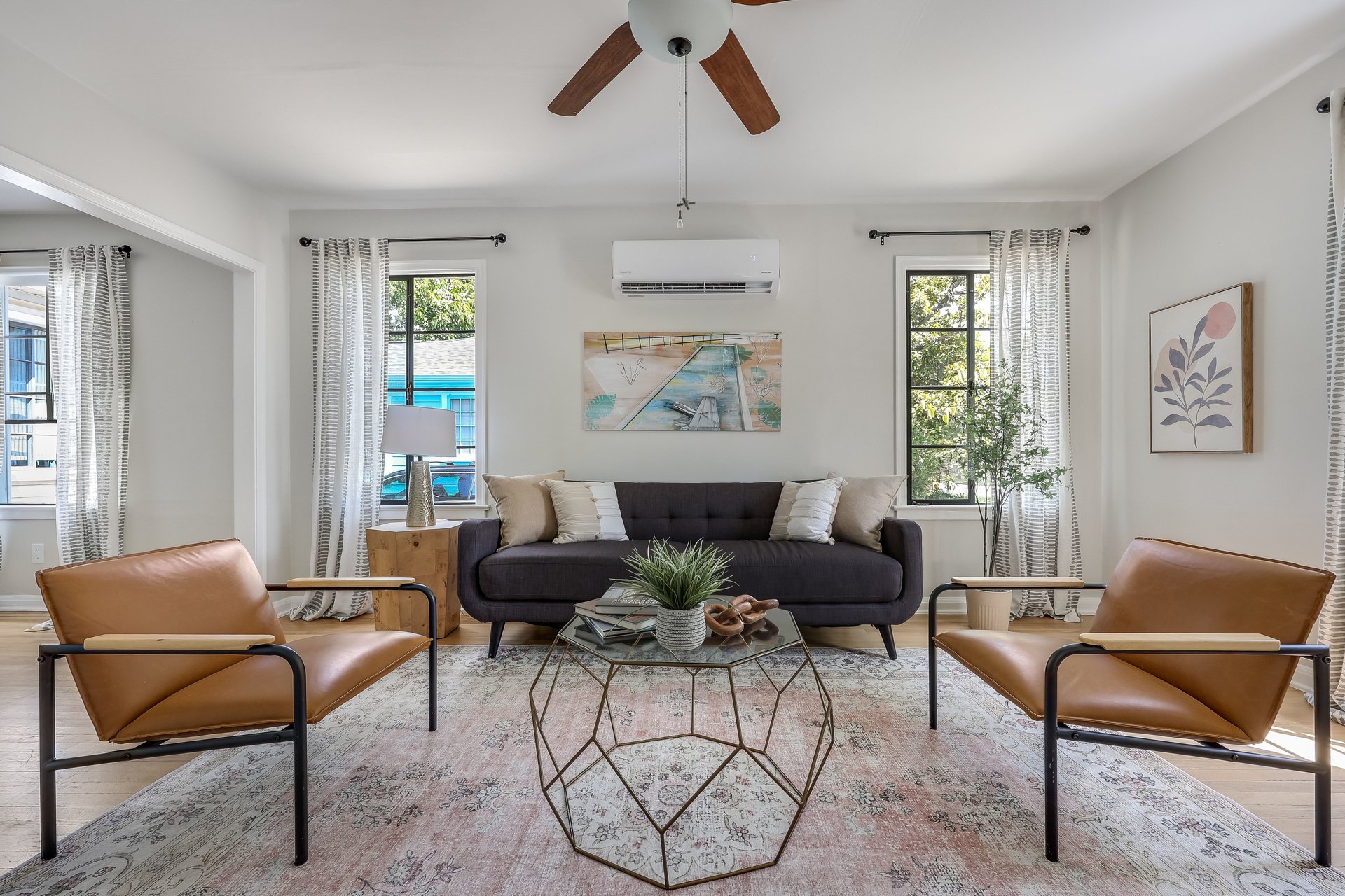 Living room with a dark sofa, tan leather chairs, and a geometric glass coffee table.