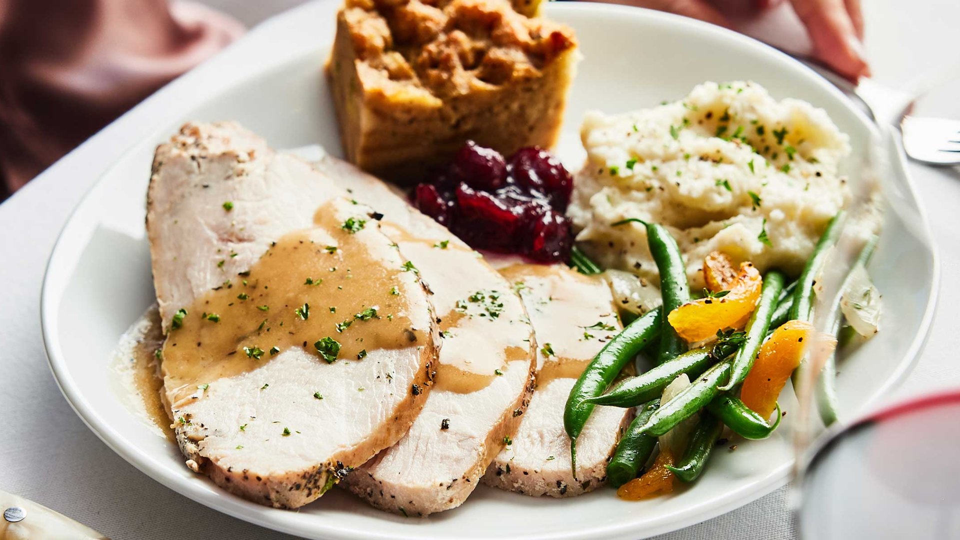 Thanksgiving dinner plate with sliced turkey, mashed potatoes, green beans, cranberry sauce, and stuffing by The Edit Real Estate