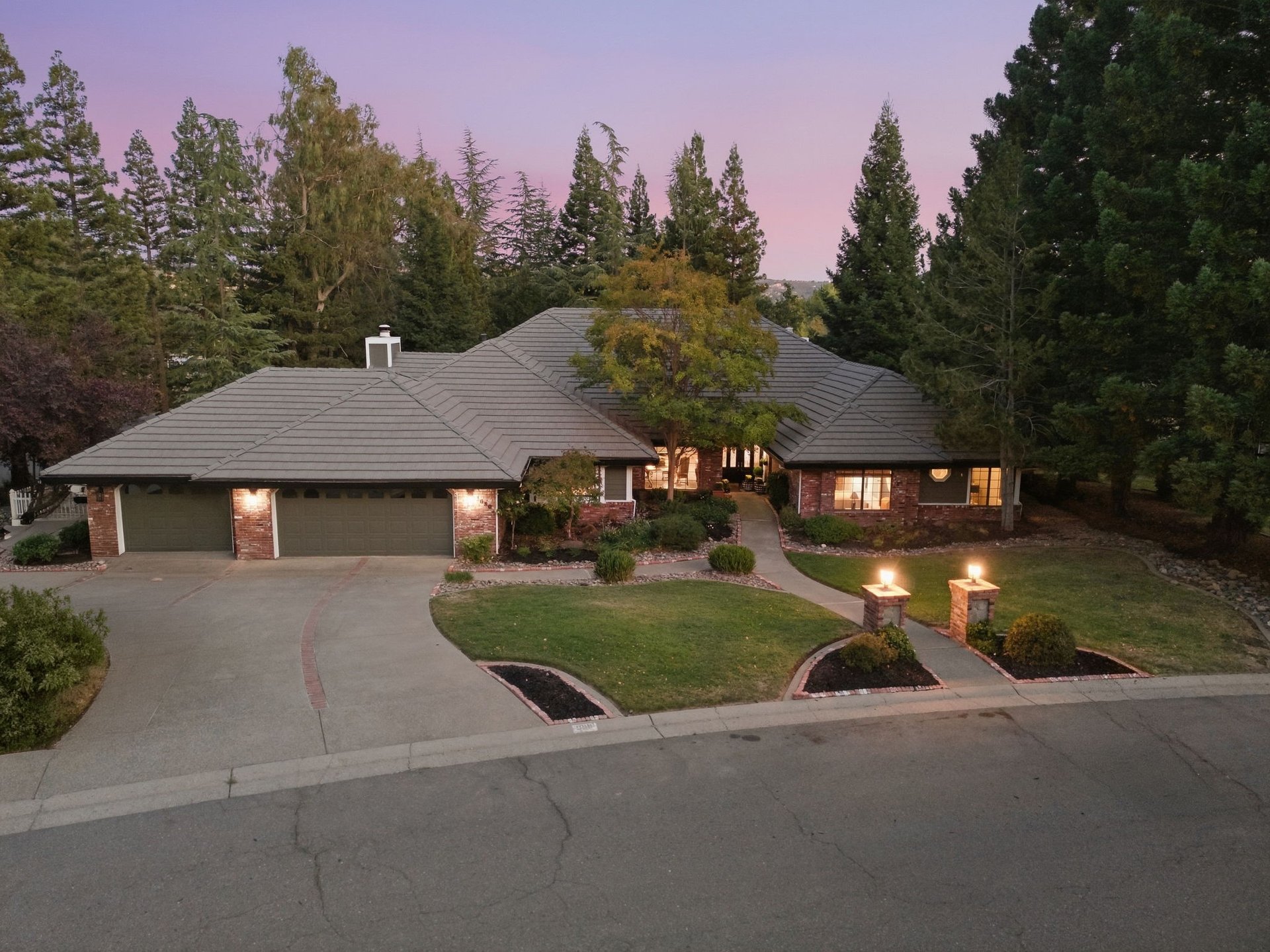 Single-story brick home with a broad tile roof, double garage, and landscaped entry at dusk.