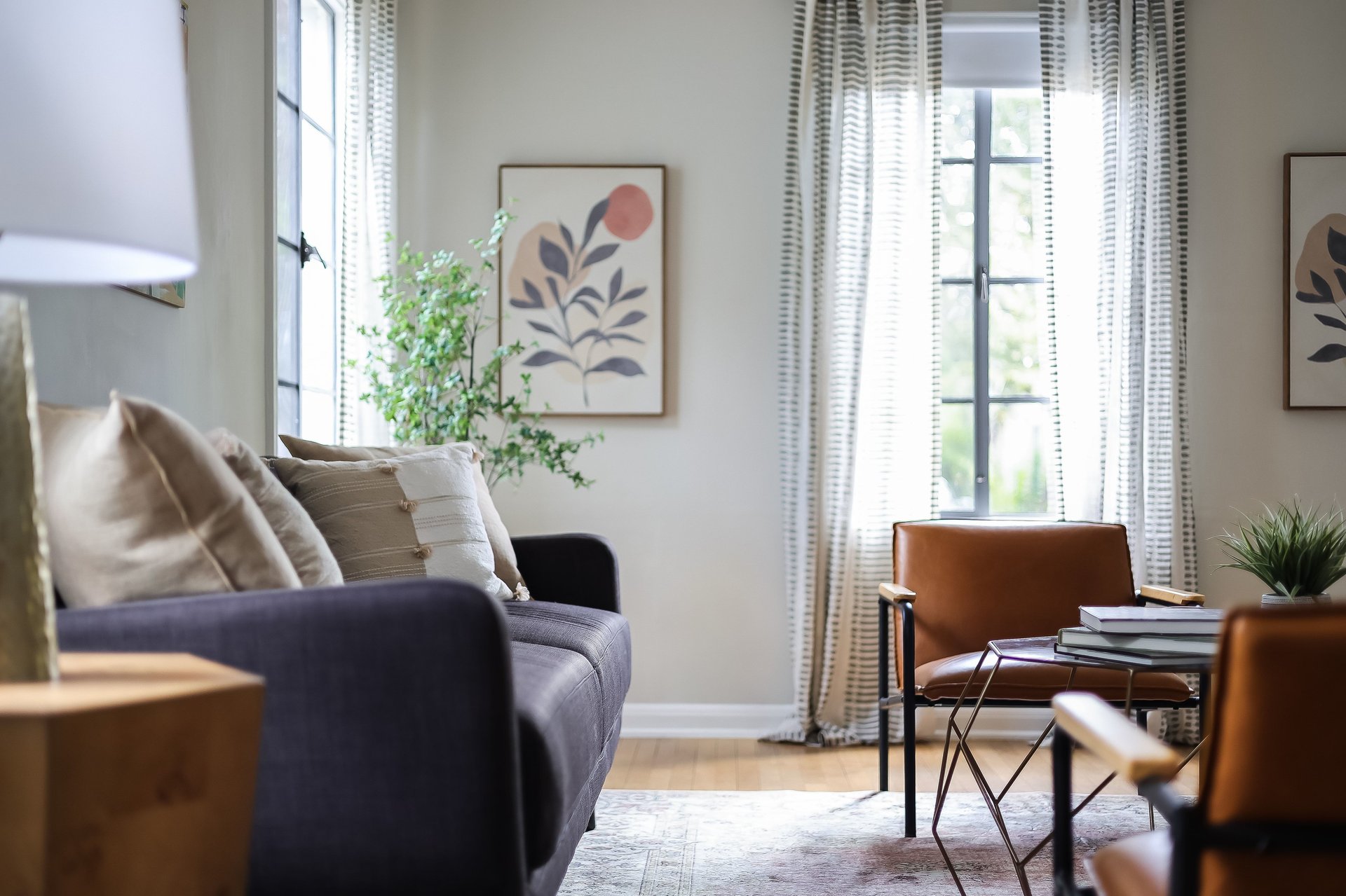 Living room with a dark sofa, leather chair, and tall curtained windows.