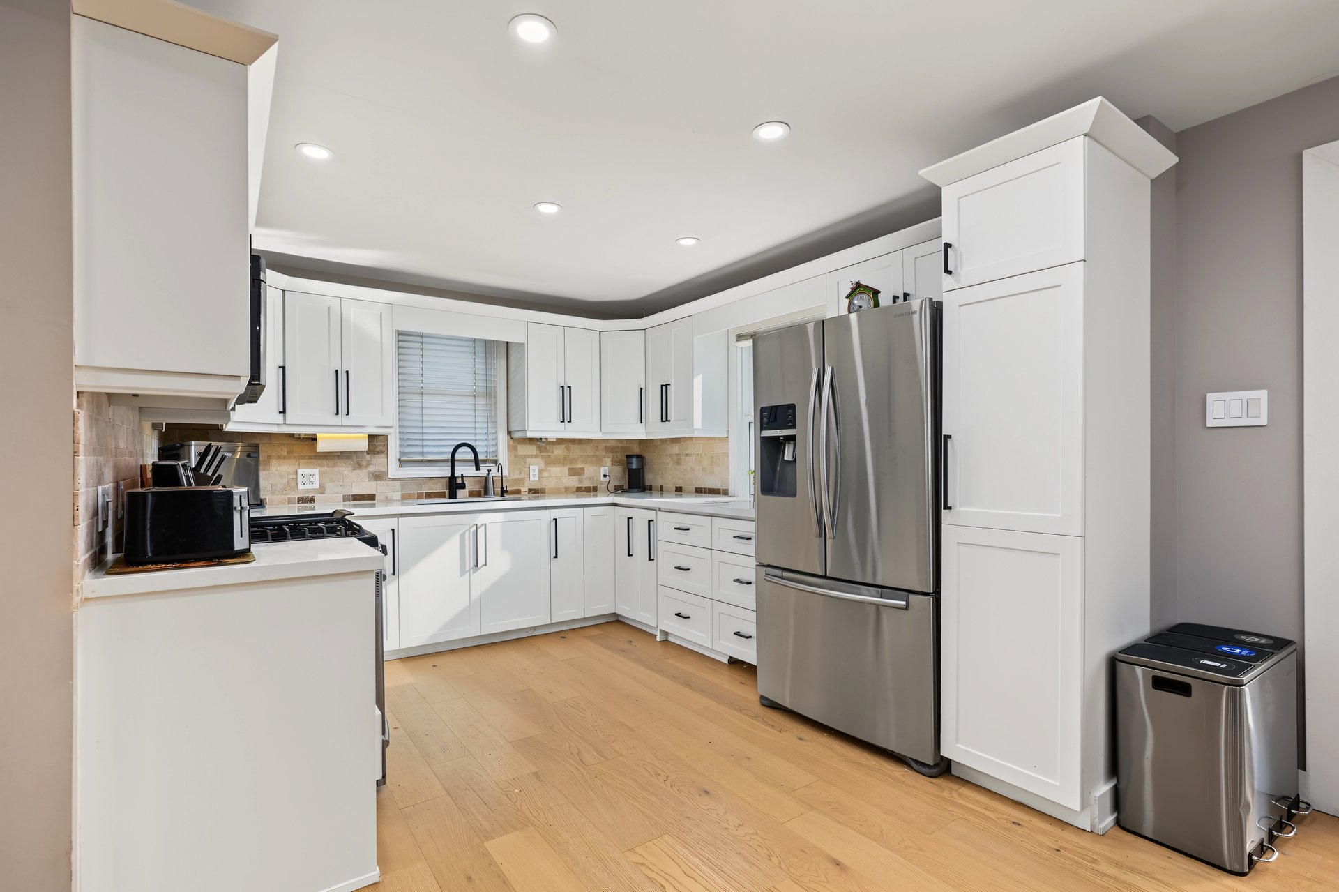 Kitchen with white cabinets, stainless steel appliances, beige tile backsplash, and light wood flooring.