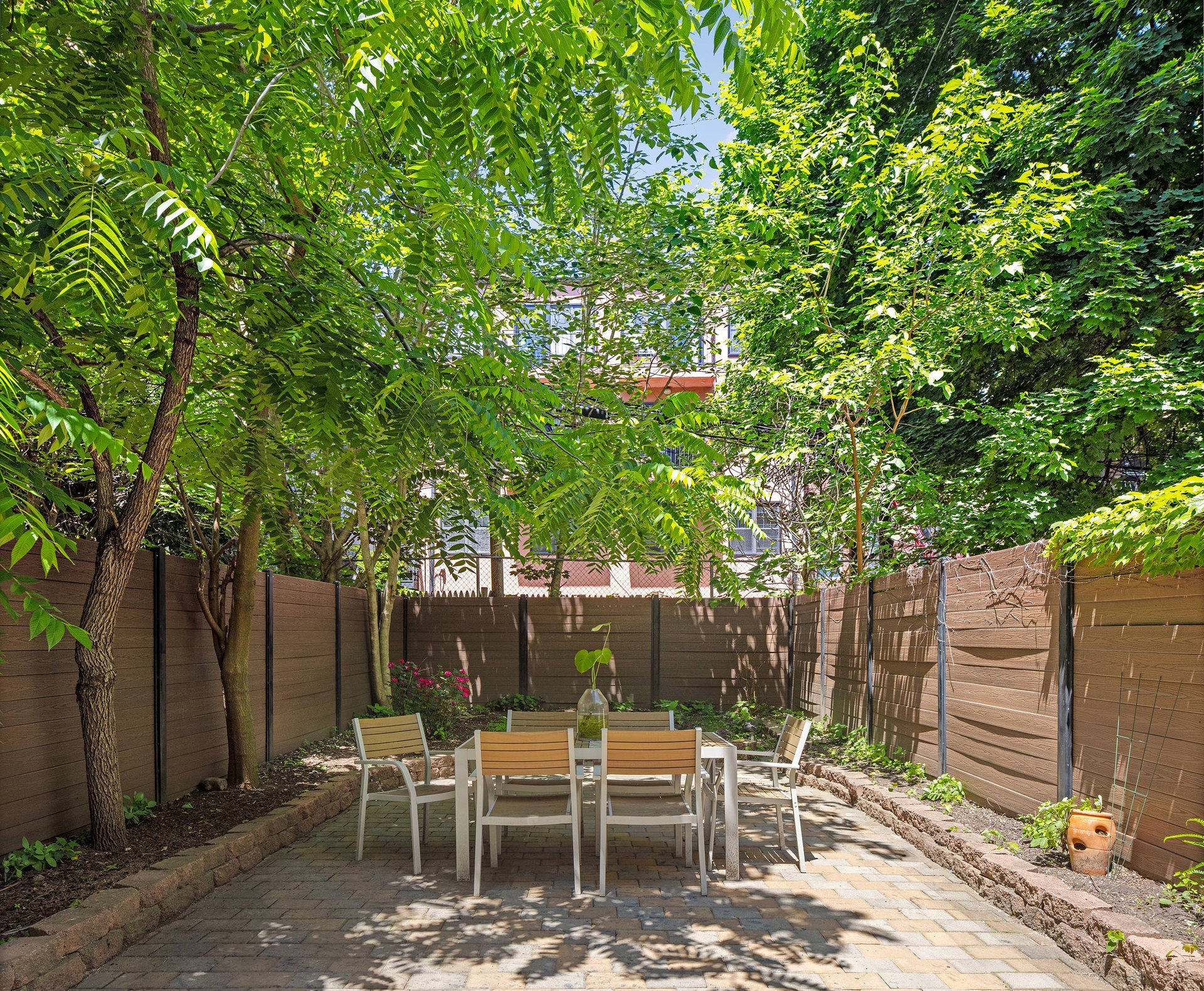 The rear garden at 457 Lexington Avenue, with a dining table beneath leafy trees.