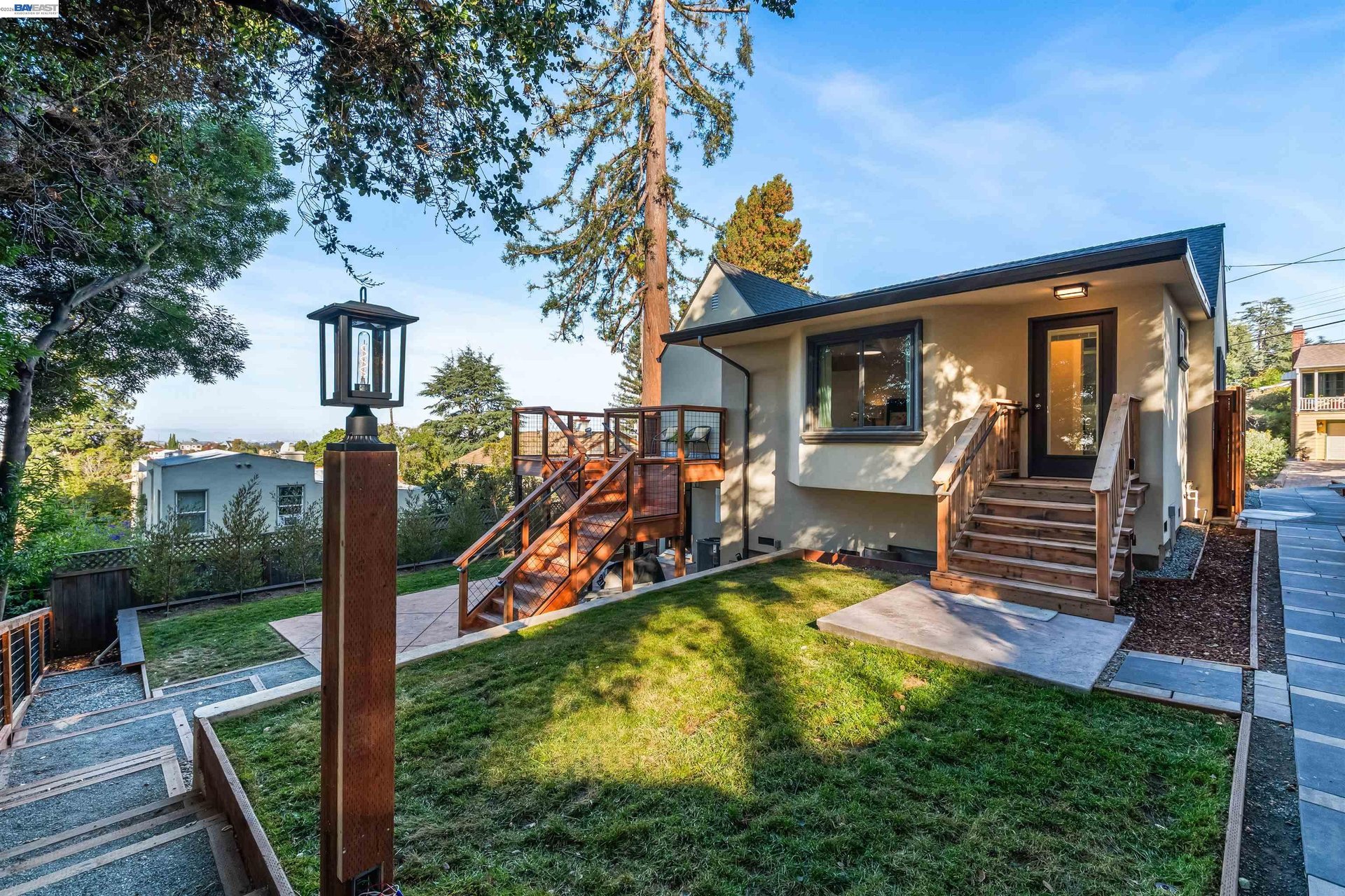 Home exterior with wooden steps, deck, landscaped lawn, and mature trees.