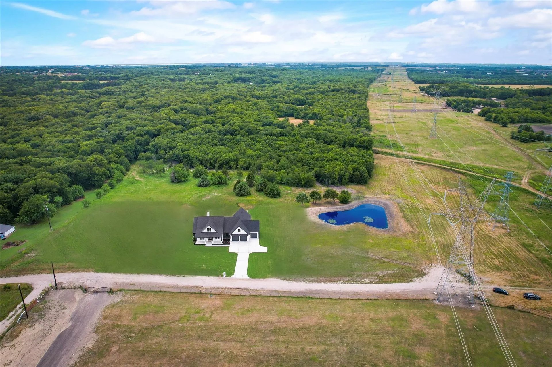 Aerial view of a home, lawn, pond, woods, and nearby power lines.