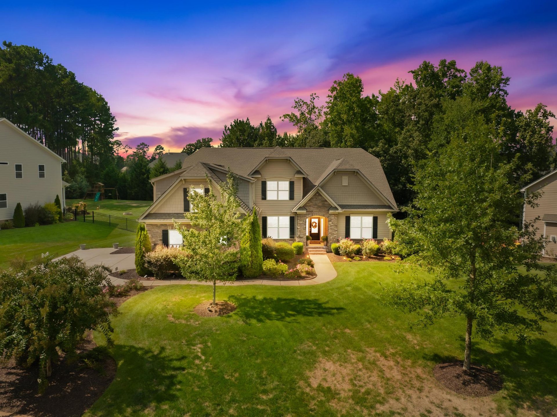 Two-story home with stone accents and landscaped lawn beneath a colorful dusk sky.