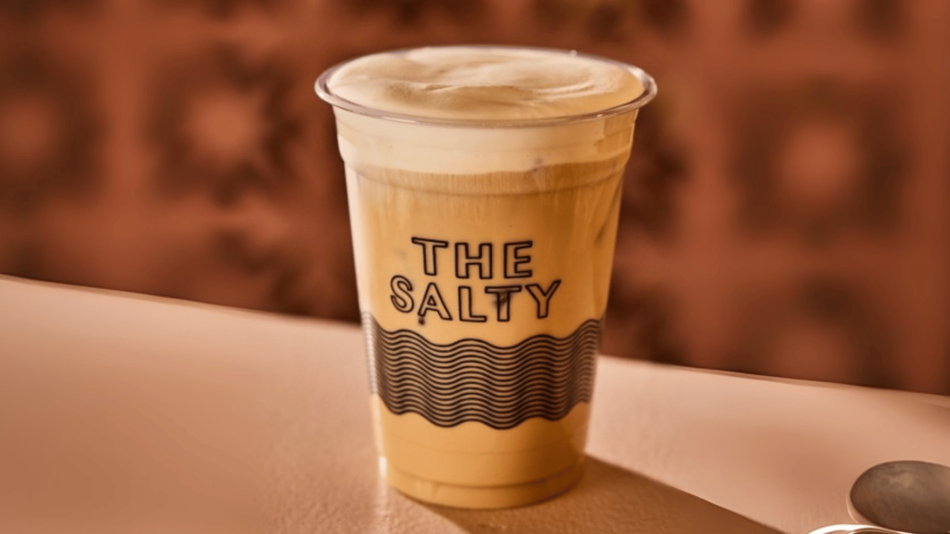 The Salty coffee cup with layered latte and wave design branding - Miami specialty coffee shop featured by The Edit Real Estate