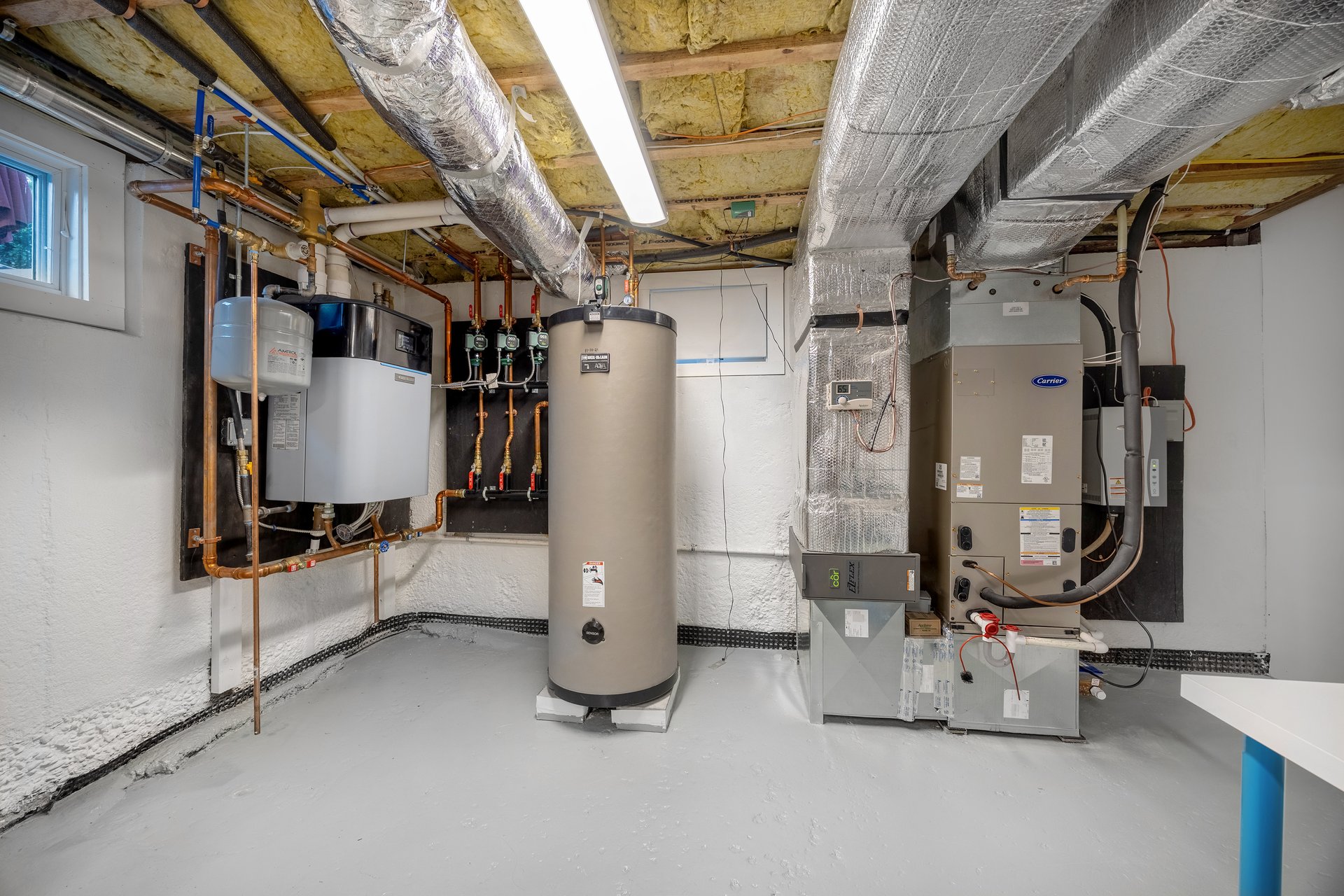 Basement mechanical room with a large water heater, HVAC units, and exposed insulated ductwork.