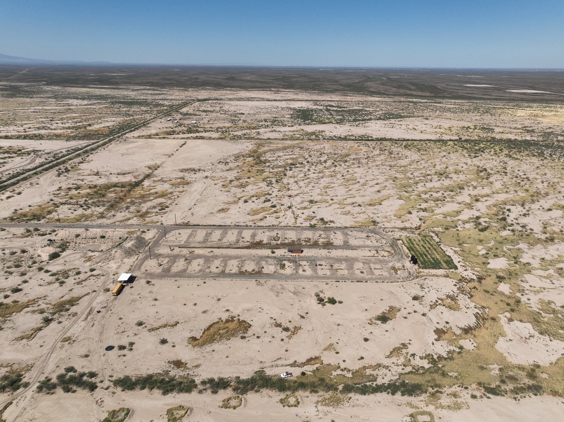 Aerial view of a sandy, sparsely vegetated property with a long graded rectangular area and dirt tracks.