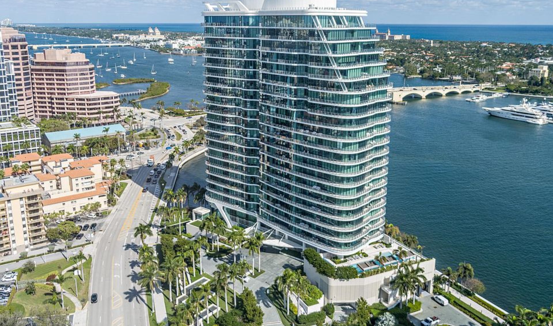 Waterfront glass condominium tower with curved balconies, yachts, and a bridge in West Palm Beach.