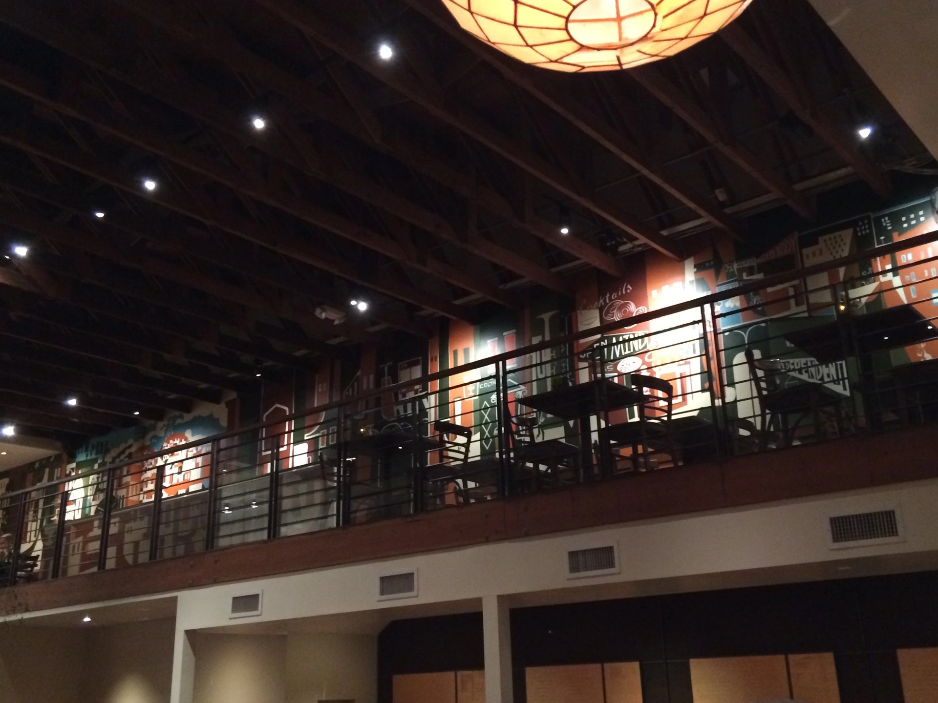 Interior of Nopa in San Francisco with a high wood-beam ceiling, warm pendant lighting, and a mezzanine lined with tables and chairs.