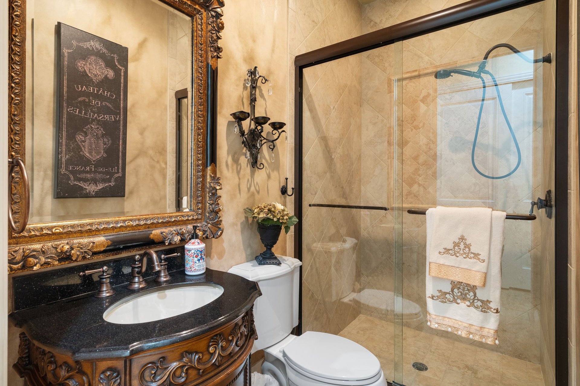 Bathroom with an ornate carved vanity, gold-framed mirror, and glass-enclosed tiled shower.