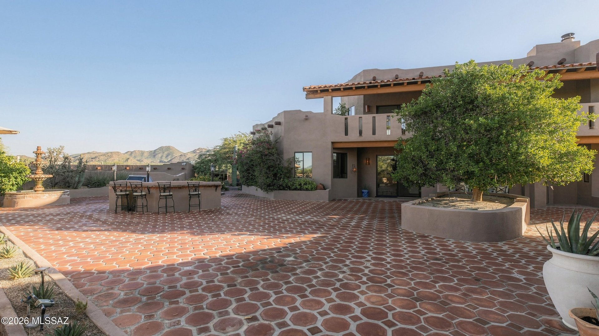 Southwestern home courtyard with terracotta paving, outdoor bar, fountain, and distant mountains.
