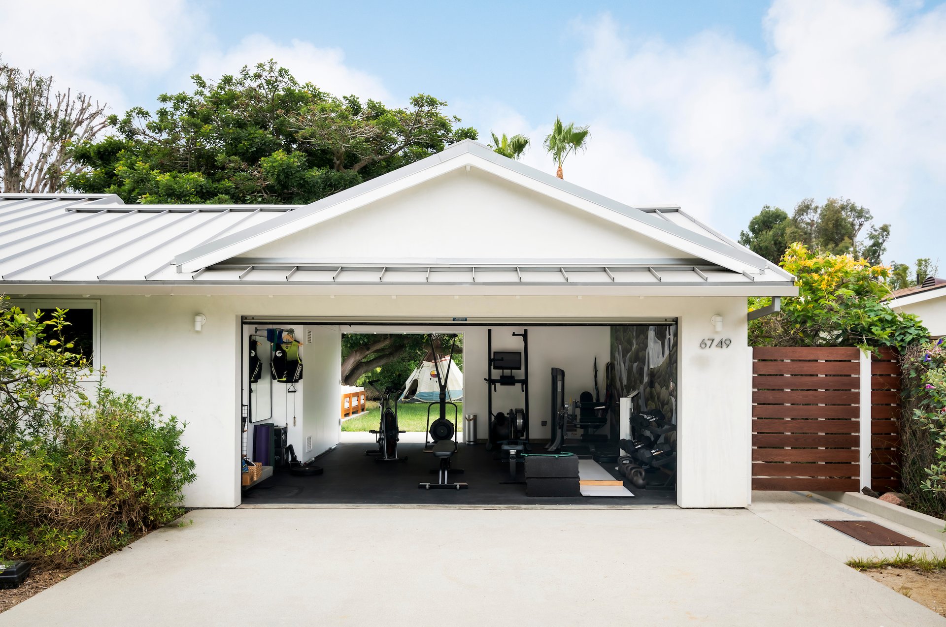 White home with an open garage gym, metal roof, and driveway.