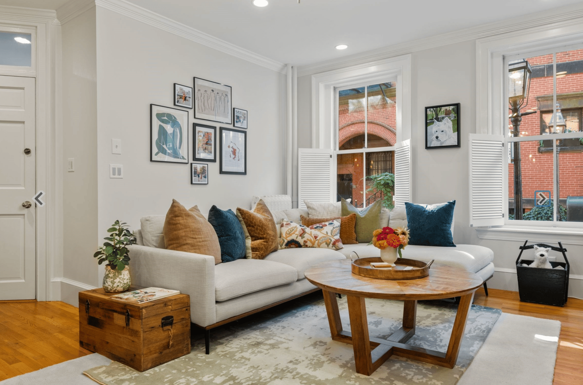 Living room with a white sectional, colorful pillows, and tall windows overlooking a brick courtyard.