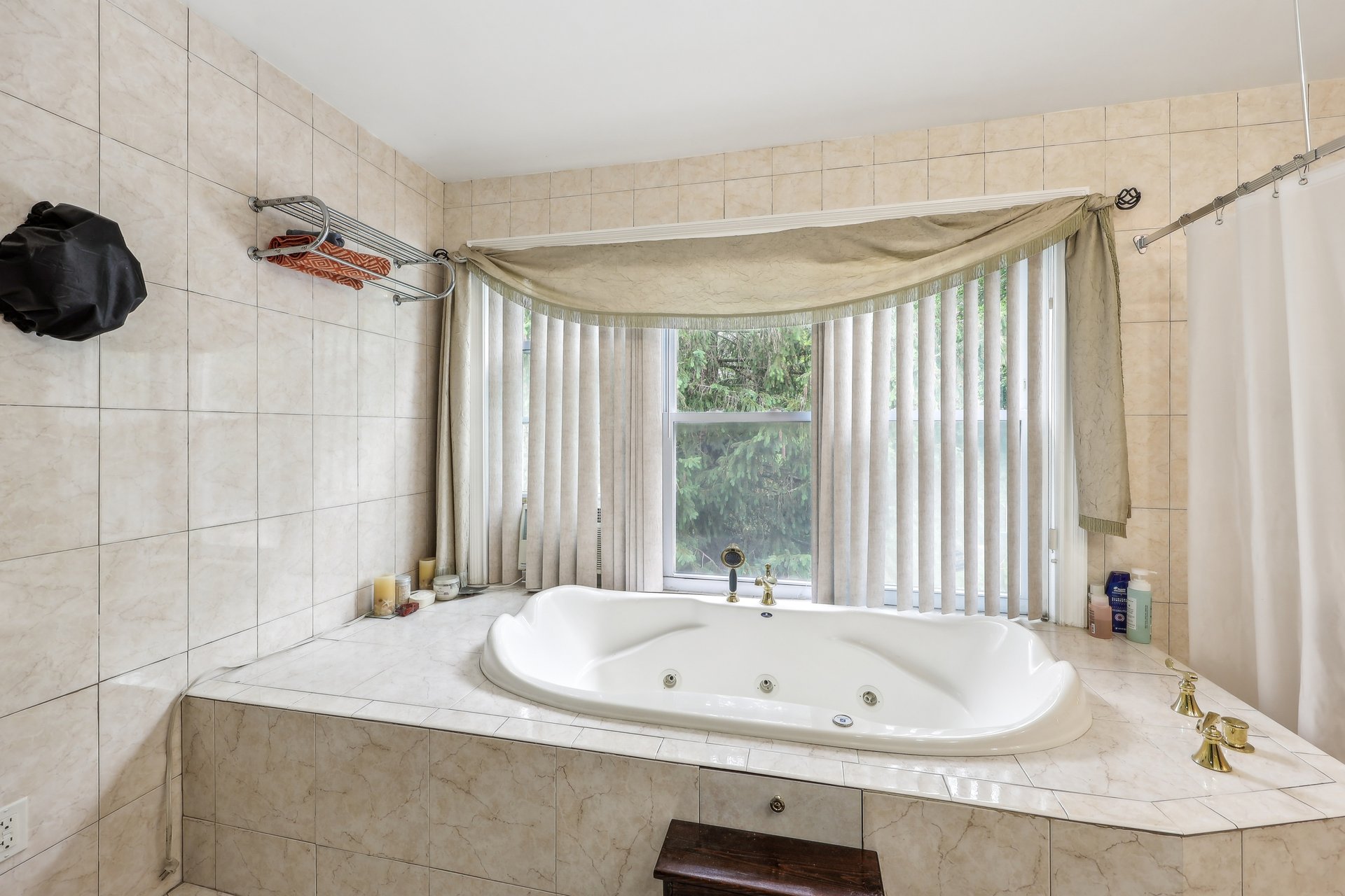Tiled bathroom with a built-in whirlpool tub beneath a wide window overlooking evergreen trees.
