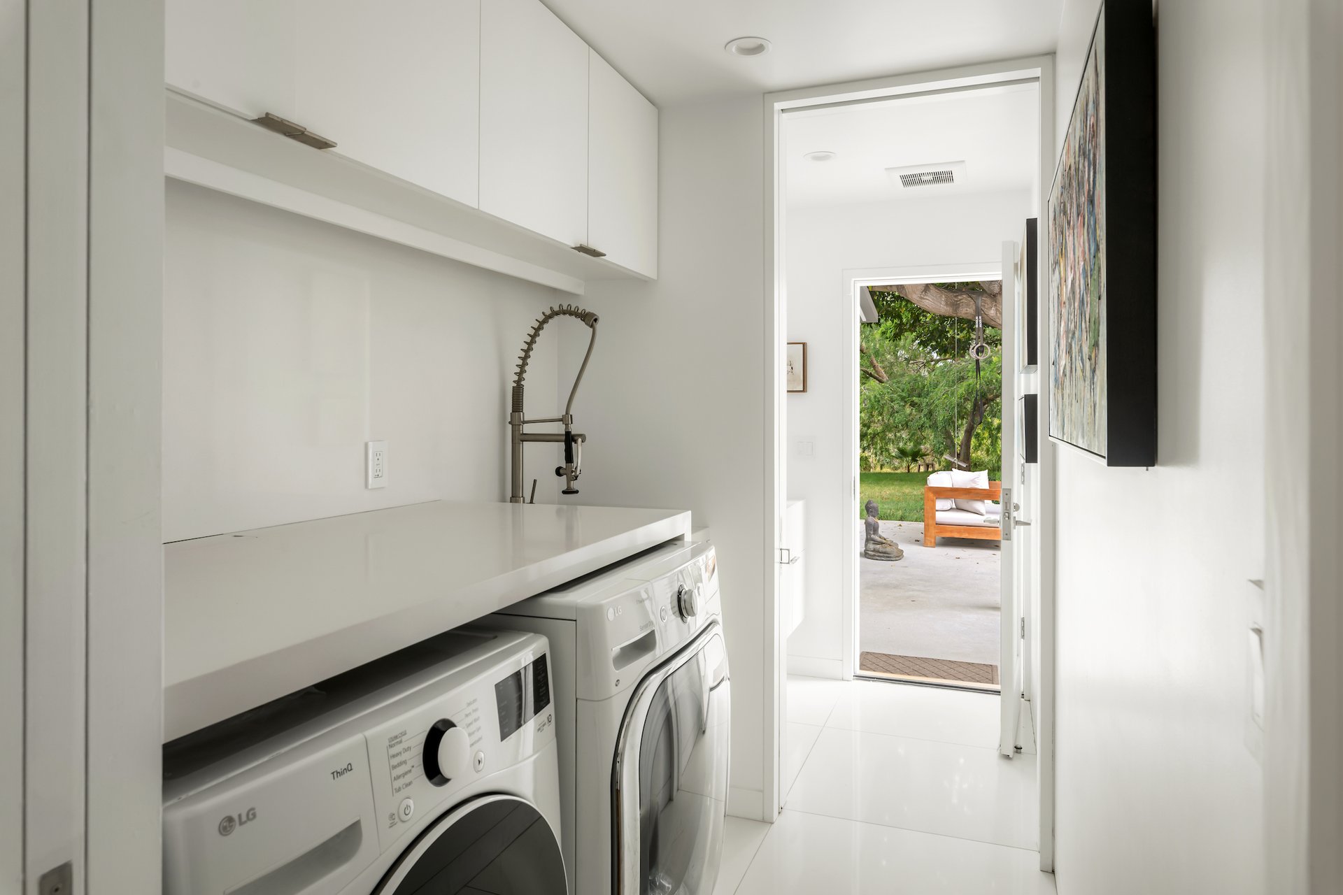 Laundry room with white cabinets, a countertop, and front-loading washer and dryer opening to a garden patio.