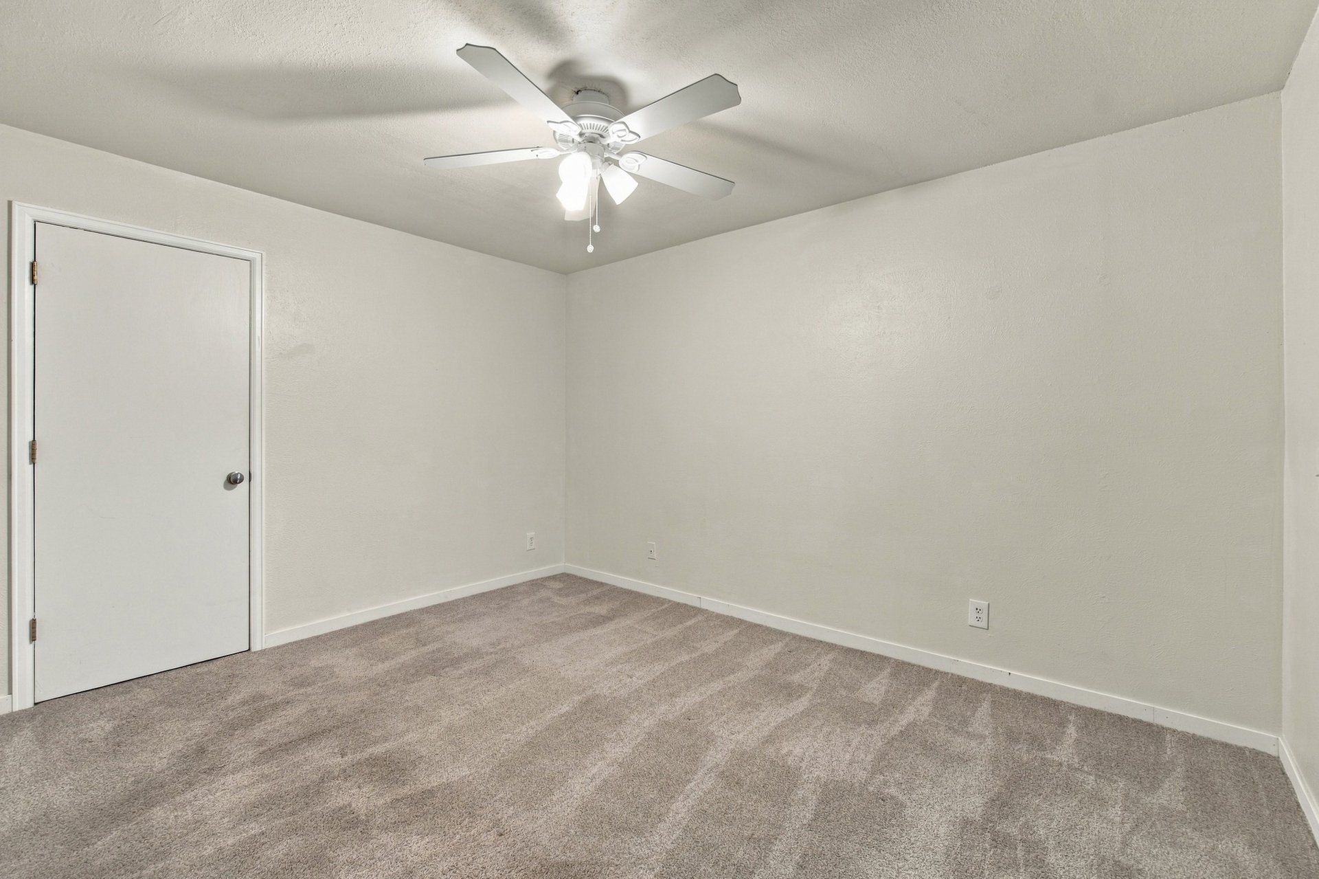 Empty carpeted bedroom with a ceiling fan and light.