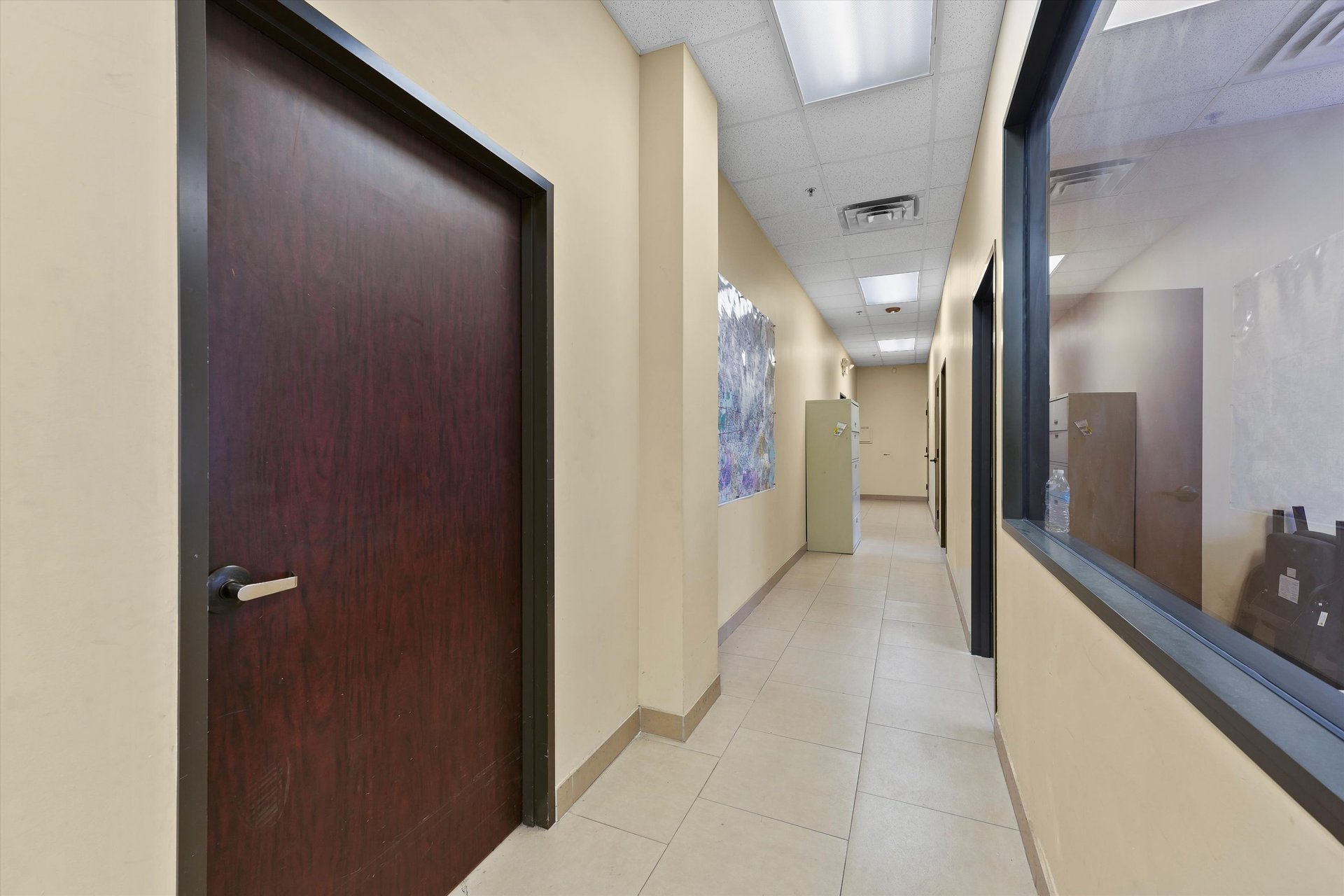 Office hallway with tiled floor, dark wood door, and glass-walled room.