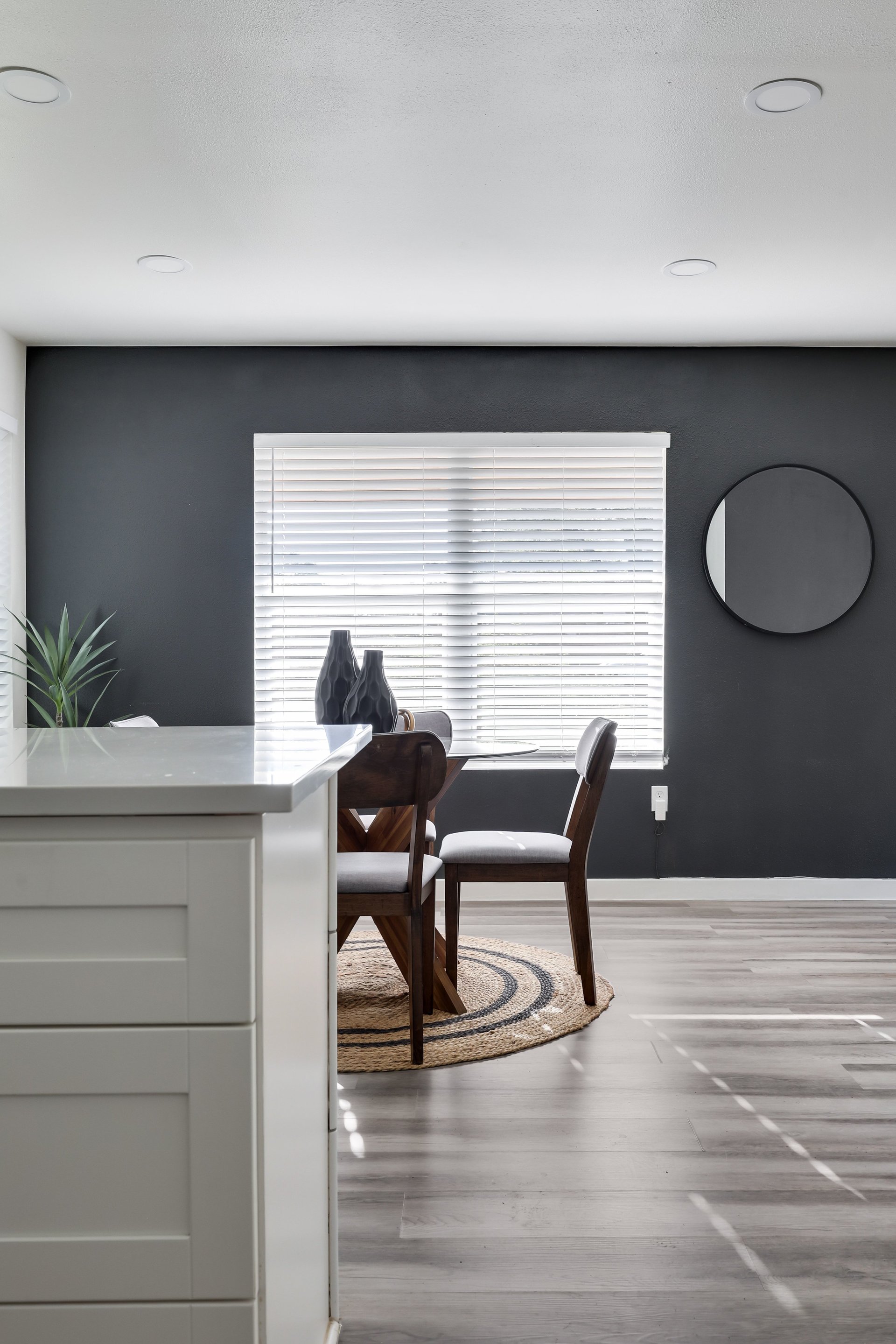 Dining area with dark wood chairs and a woven rug beside a white kitchen island.