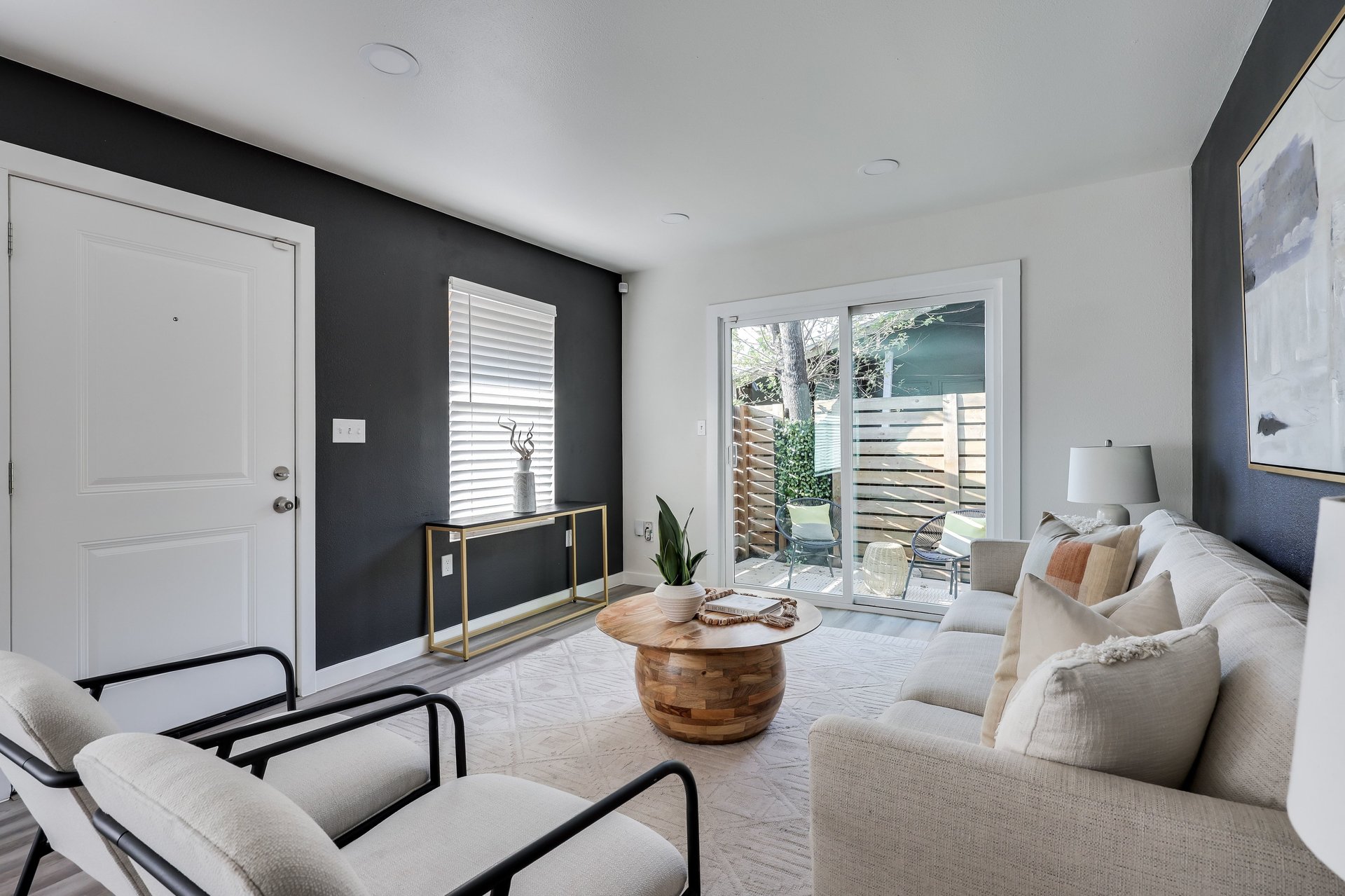 Furnished living room with a white sofa, round wooden coffee table, and sliding doors to a fenced patio.