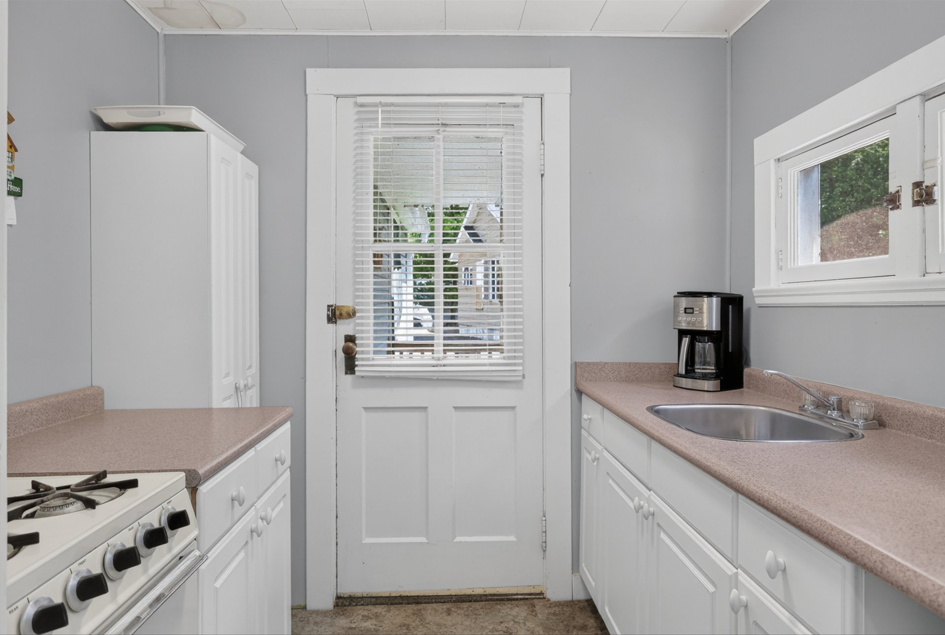 Compact kitchen with white cabinets, pink-beige counters, and a door with blinds.