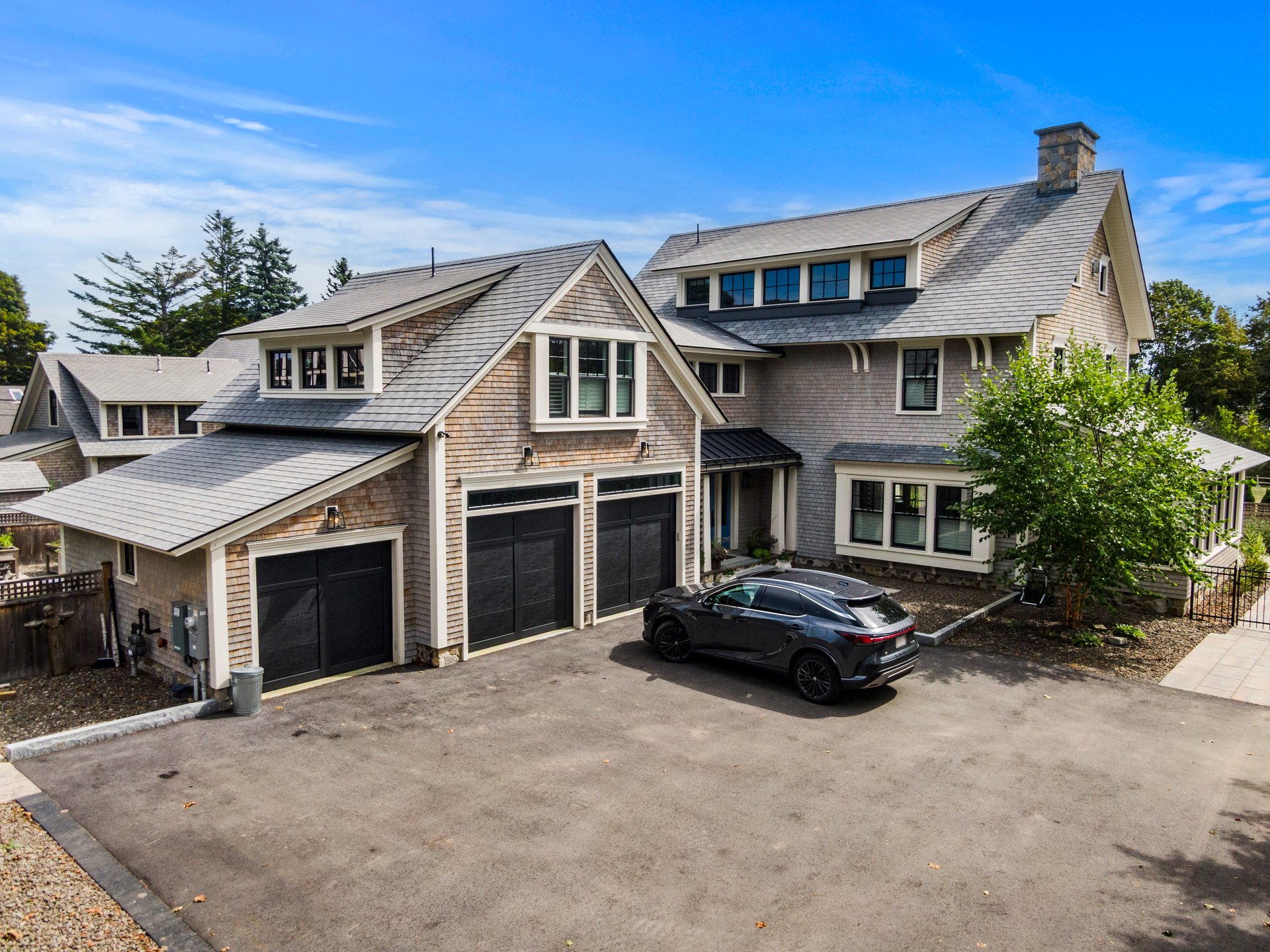 Shingle-style home with multiple garage doors and a dark car in the driveway.
