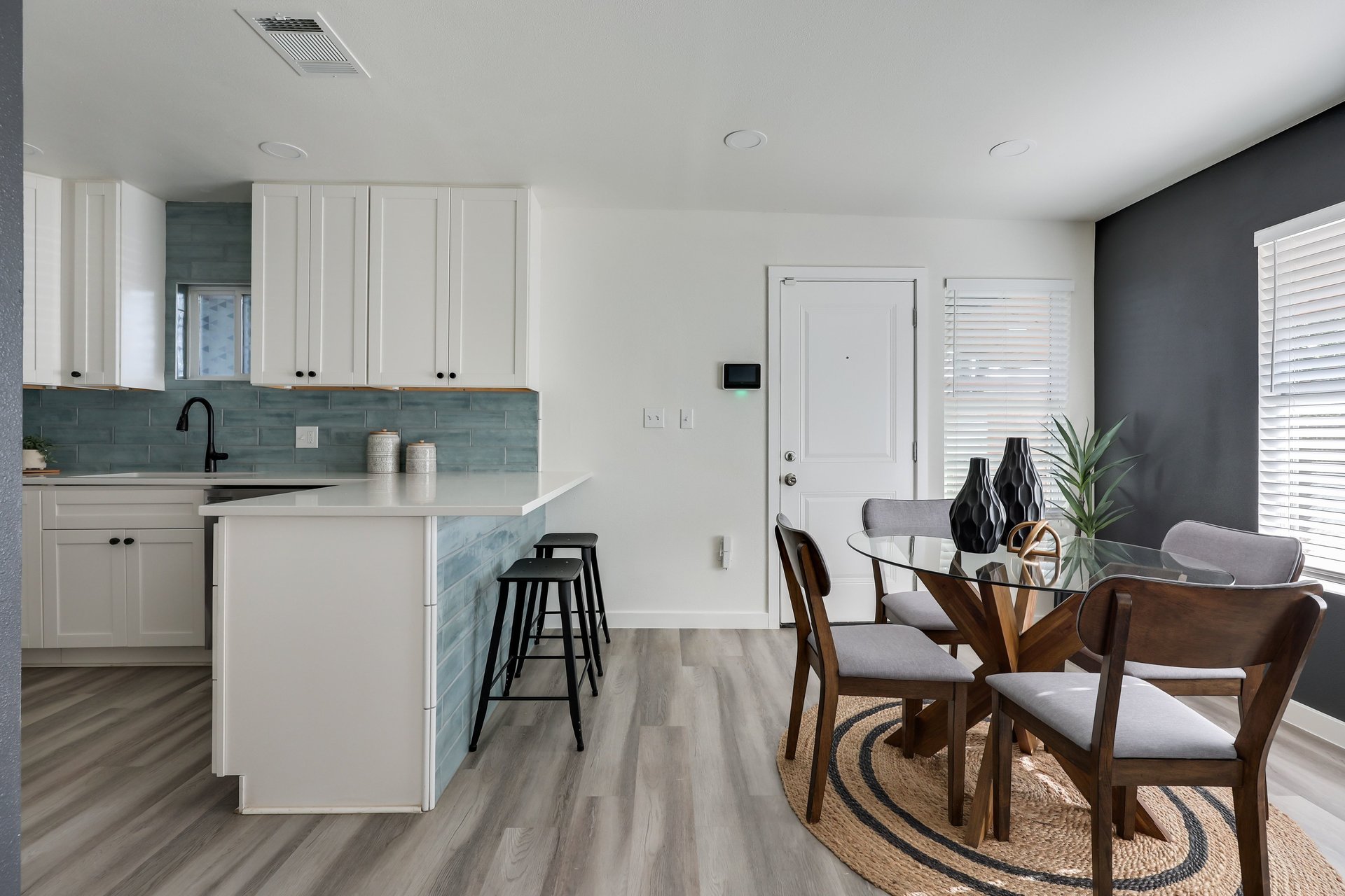 Open-plan kitchen and dining area with blue tile backsplash, white cabinets, and glass-top table.