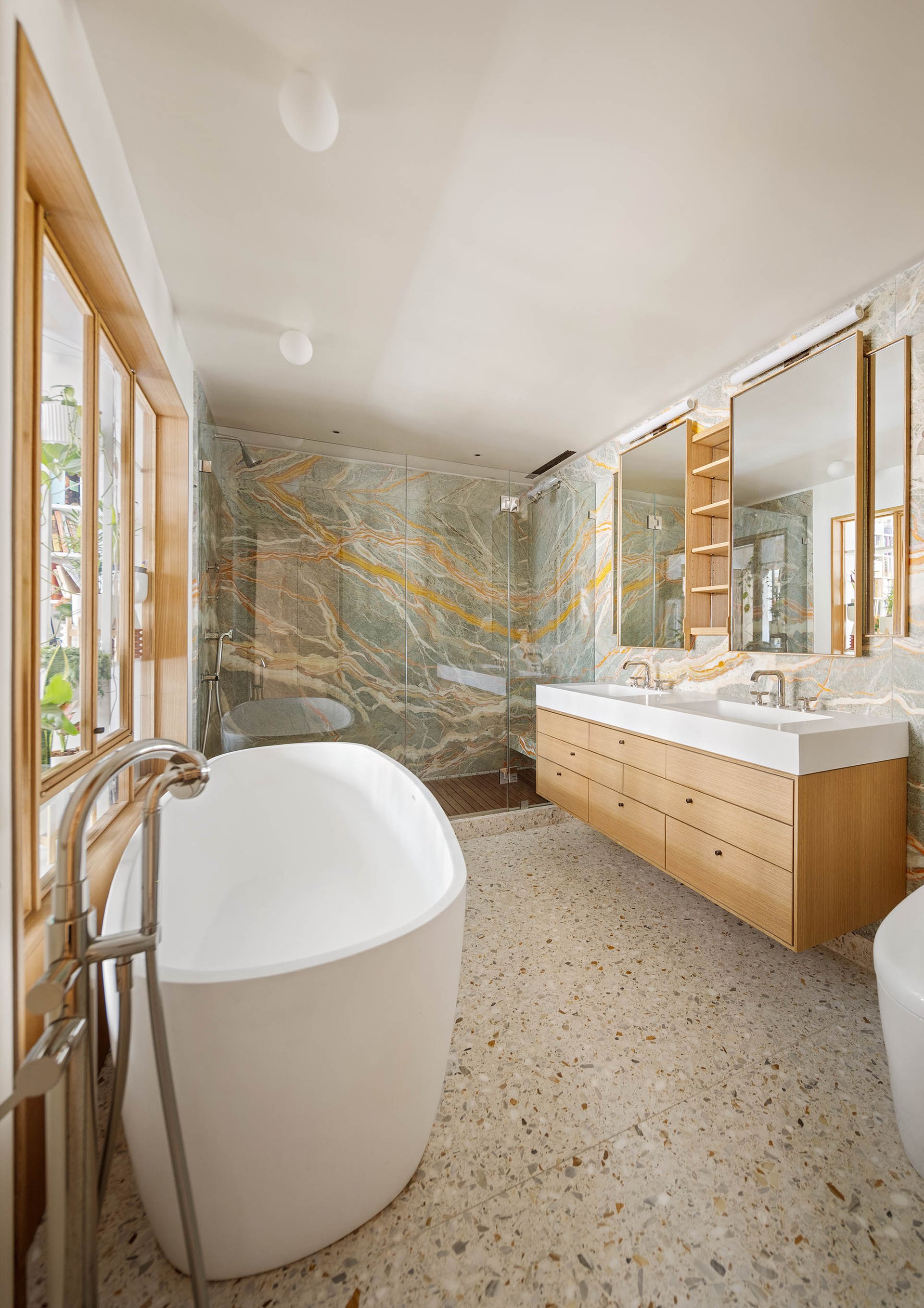 Primary bathroom at 50 Wooster Street 4NR, showing the freestanding tub, wood vanity and veined stone shower wall.