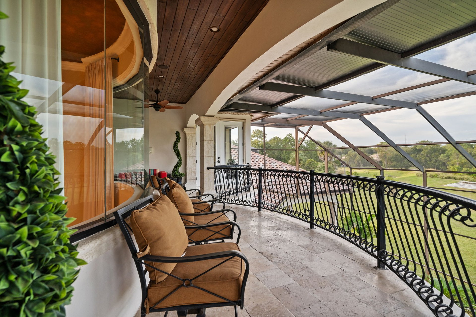 Screened-in balcony with tan lounge chairs, tiled flooring, and a view of the green grounds.