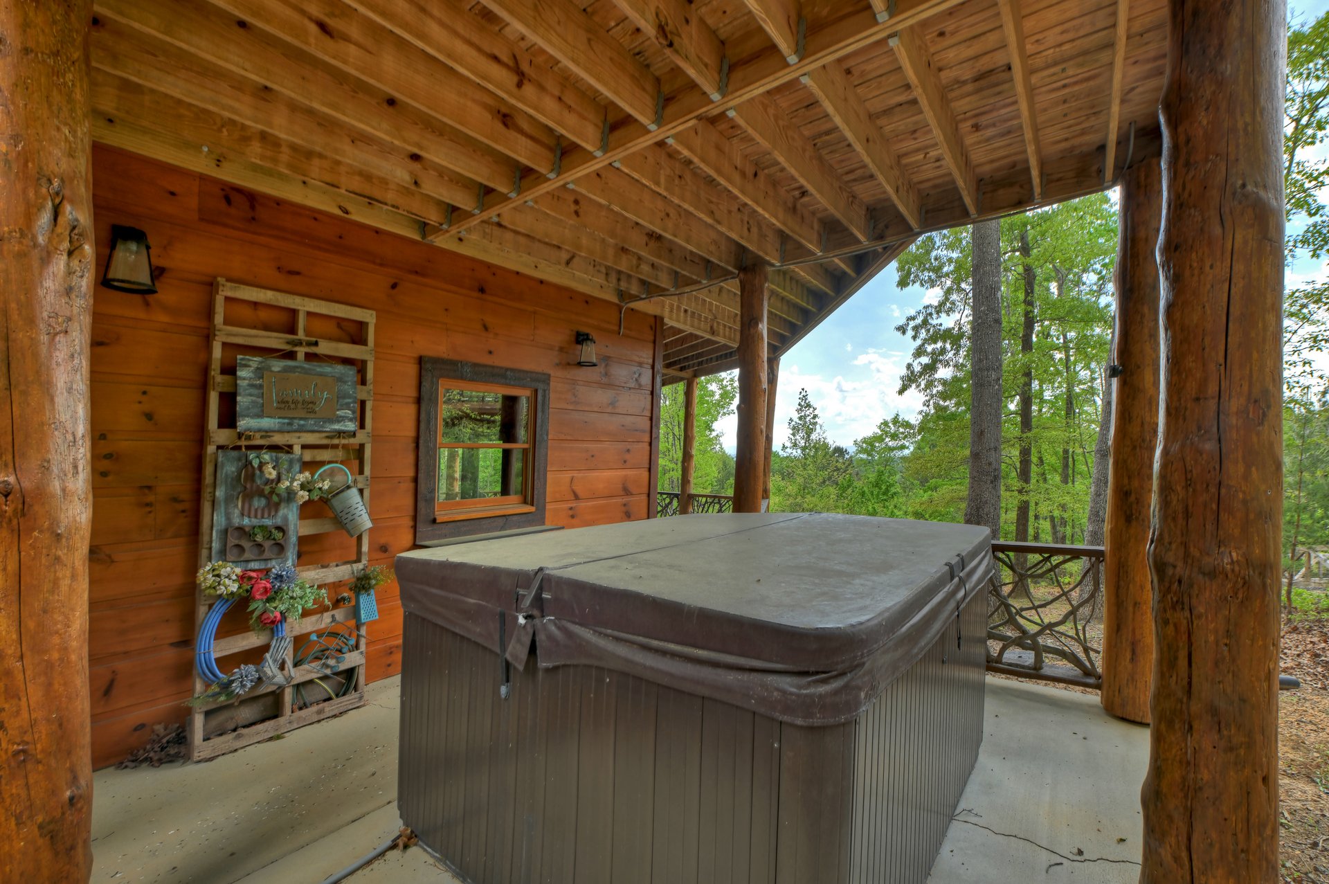 Hot tub on a covered log-post porch overlooking green woodland.