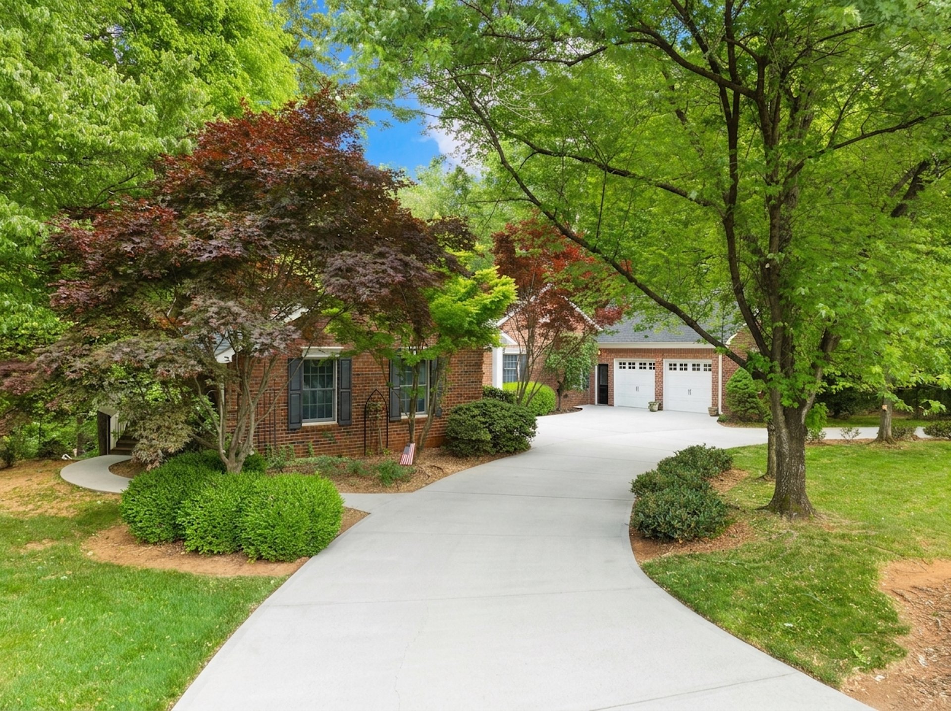 Red-brick house with a curved driveway, twin garage doors, and mature trees framing the front.